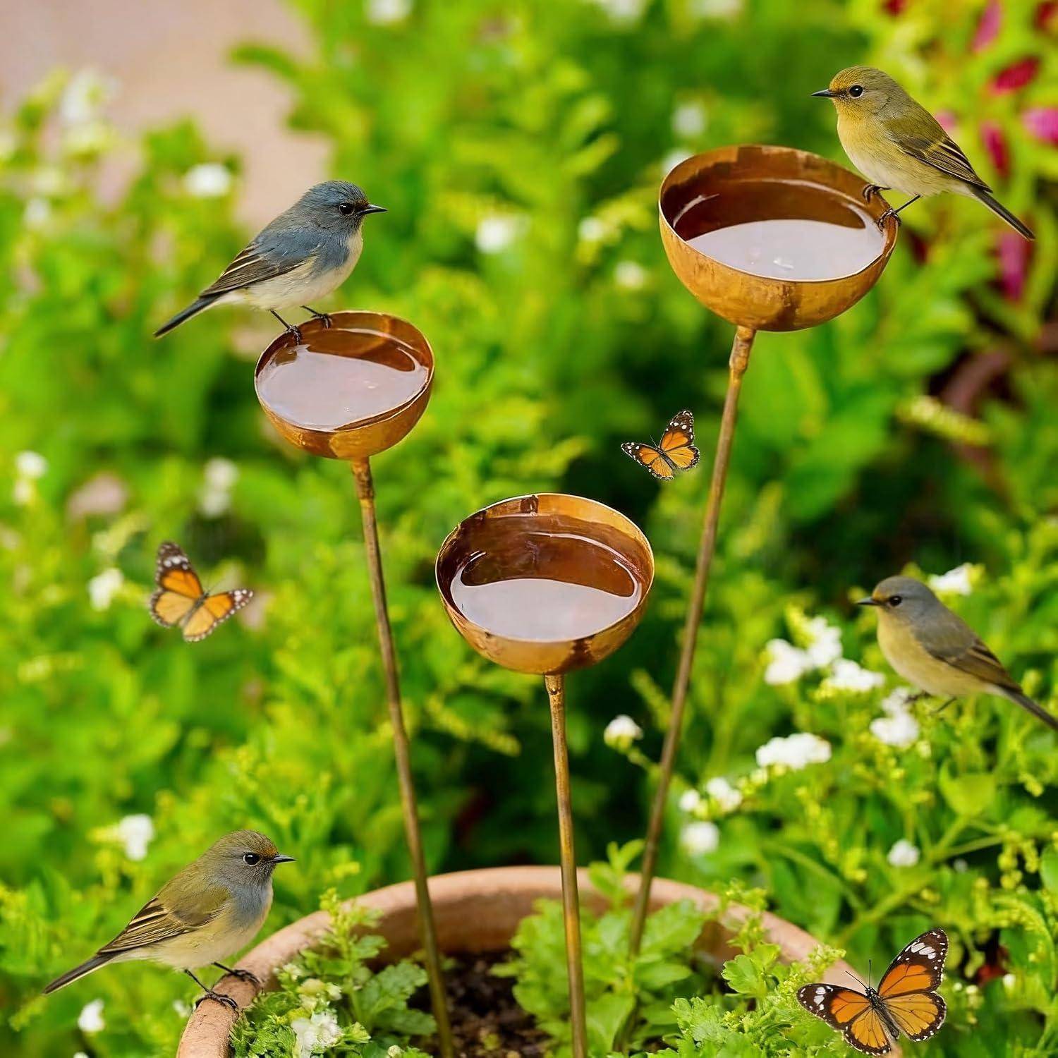 Vier kleine Vögel und mehrere Schmetterlinge versammeln sich um Kupferschalen-Futterspender in einem üppigen grünen Garten.