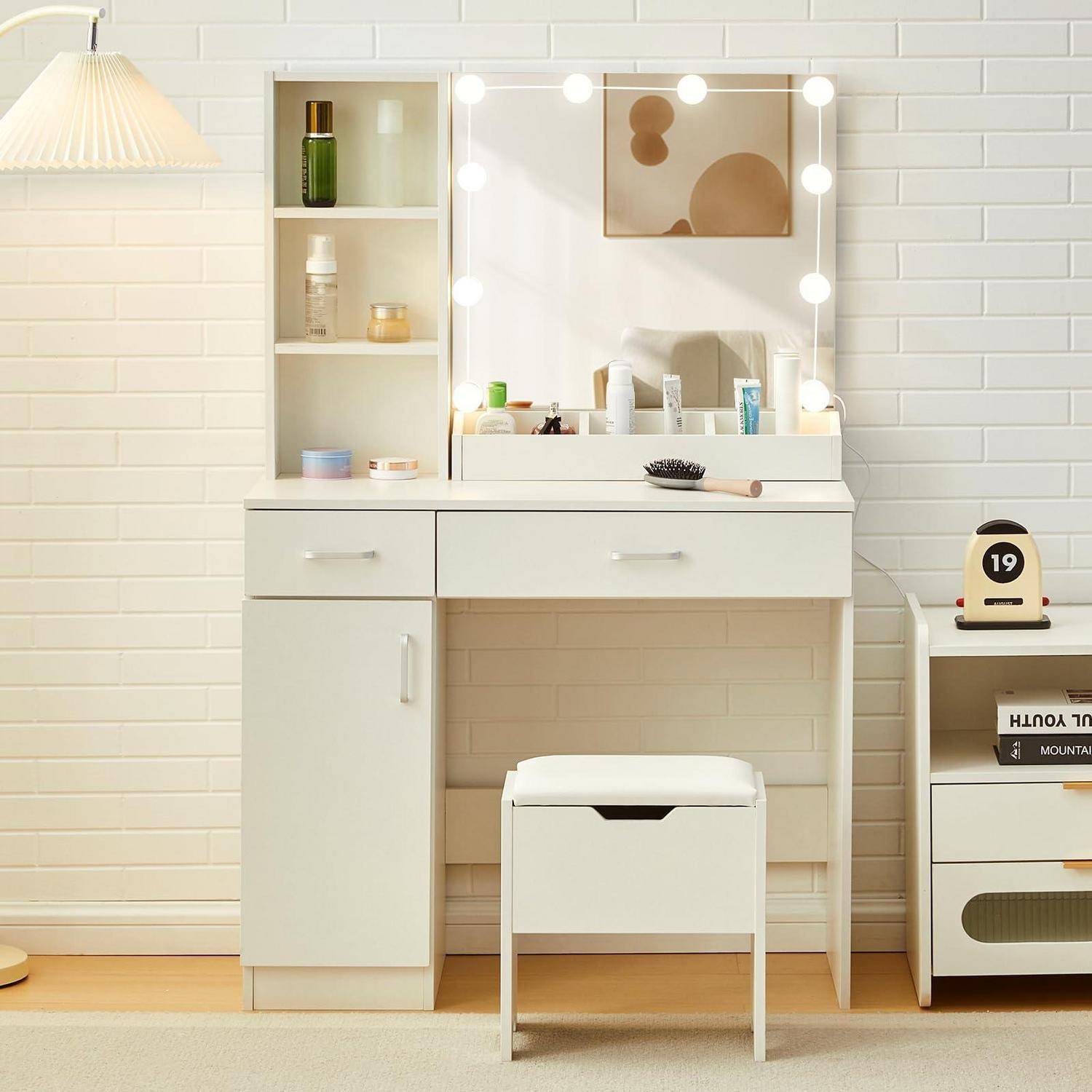 Weißer Frisiertisch mit beleuchtetem Spiegel, Regalen und Hocker in einem minimalistischen Schlafzimmer, mit einem kleinen Schrank und Deko daneben.