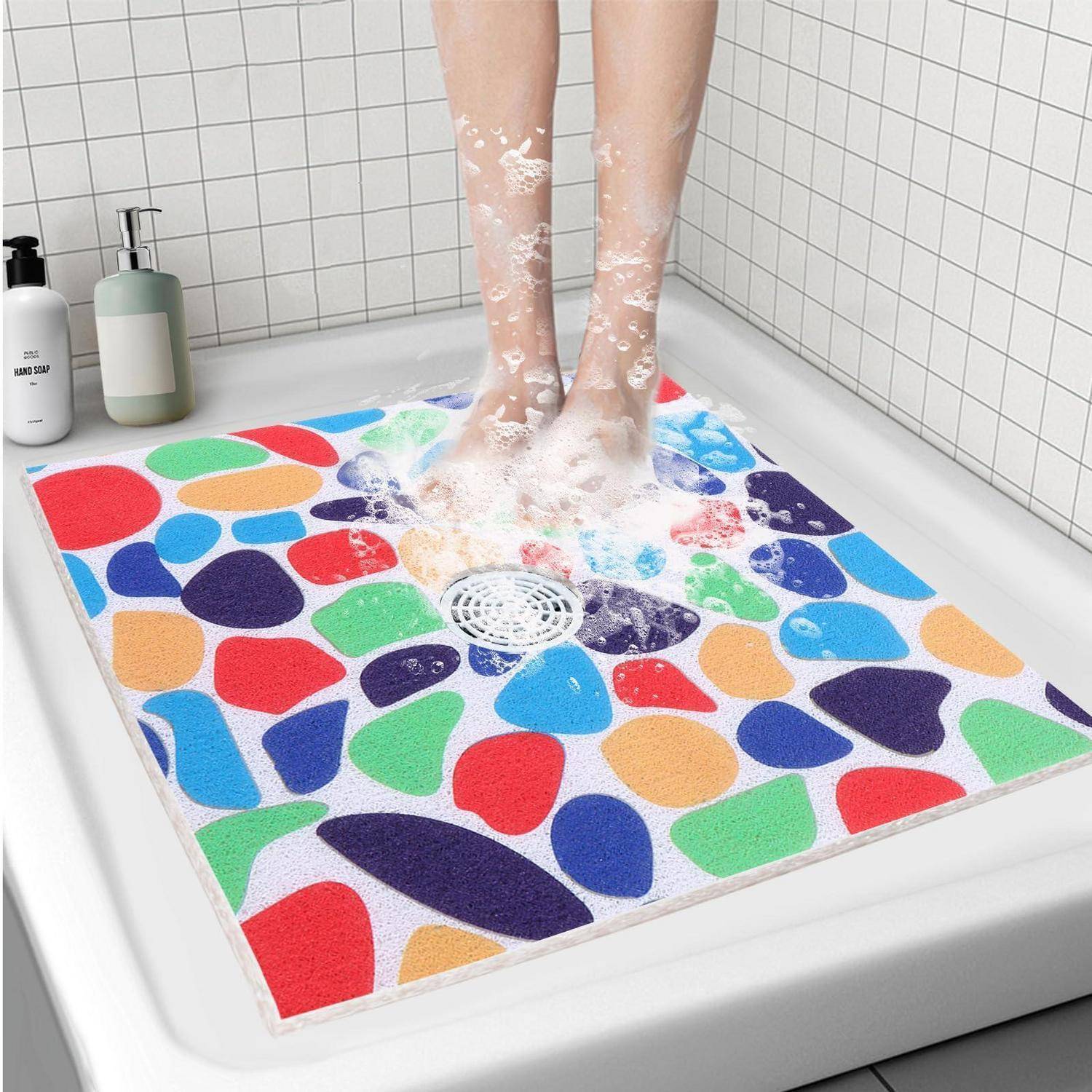 Eine Person wäscht ihre Füße auf einer farbenfrohen, saugfähigen Badematte in einer Dusche oder Badewanne, mit Seifenschaum und einer sichtbaren Abflussöffnung.