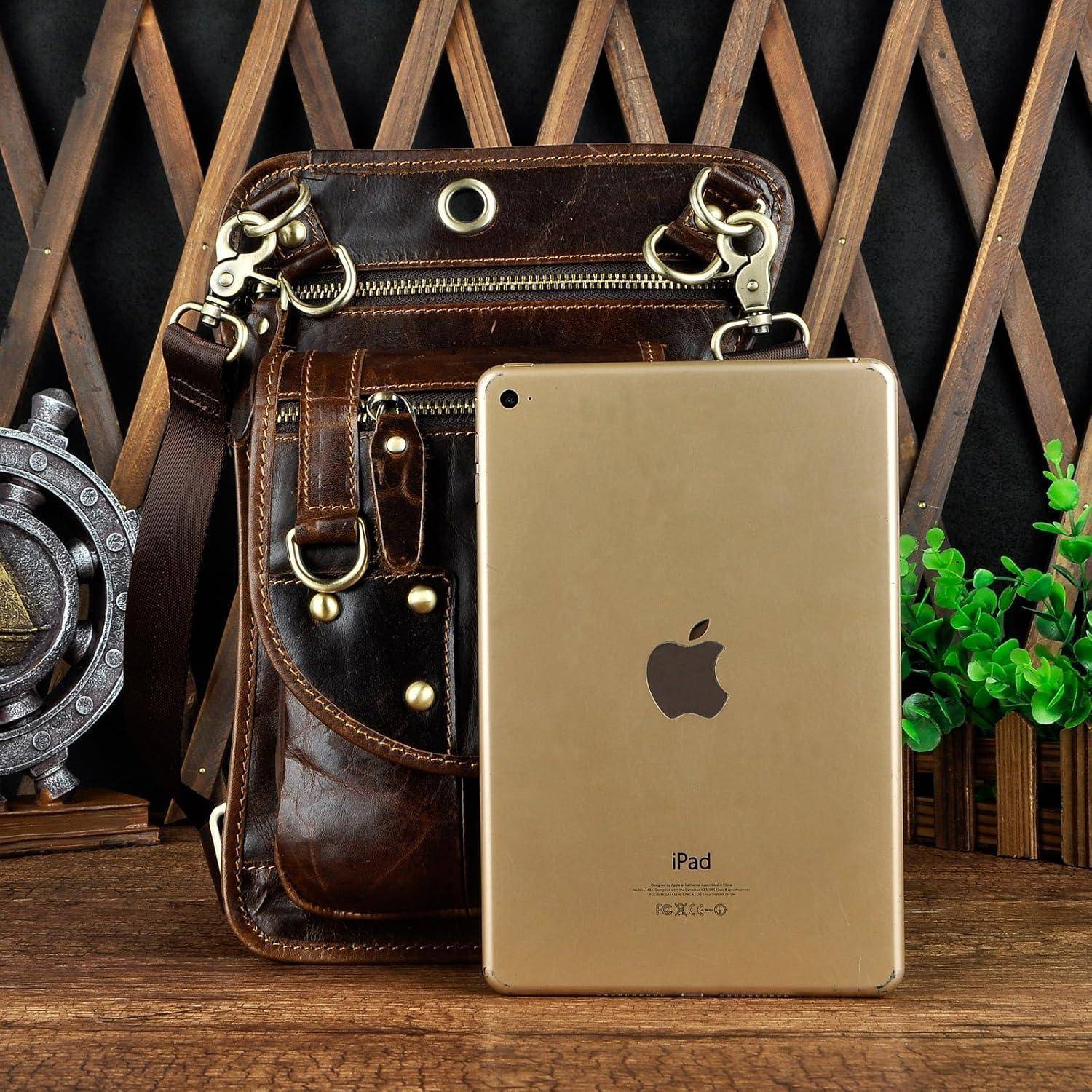 Ein goldenes iPad lehnt an einer braunen Lederschultertasche auf einem Holztisch, mit einem dekorativen Metallrad und einer Pflanze im Hintergrund.