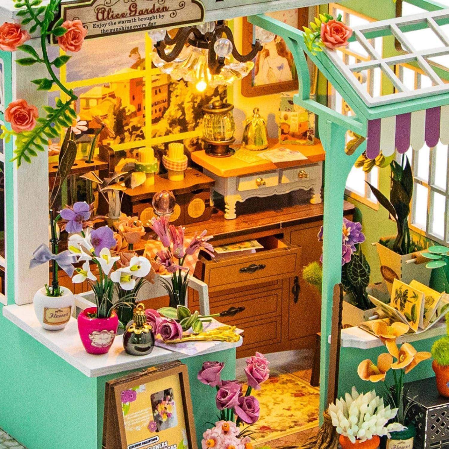 Miniatur-Blumenladen-Szenerie mit warm beleuchteter Werkbank, Topfblumen und Schnittblumen sowie einem Schild mit der Aufschrift „Alice's Garden".