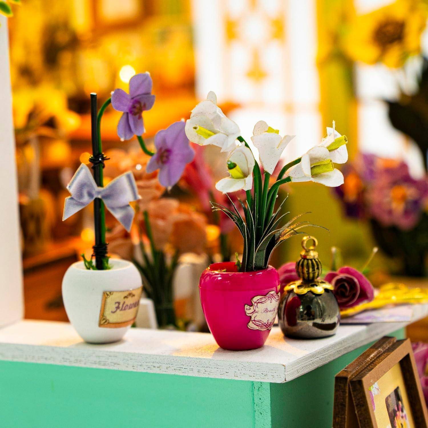 Dekorative künstliche Blumenarrangements in kleinen bunten Töpfen, die auf einem Regal im Innenraum ausgestellt sind.