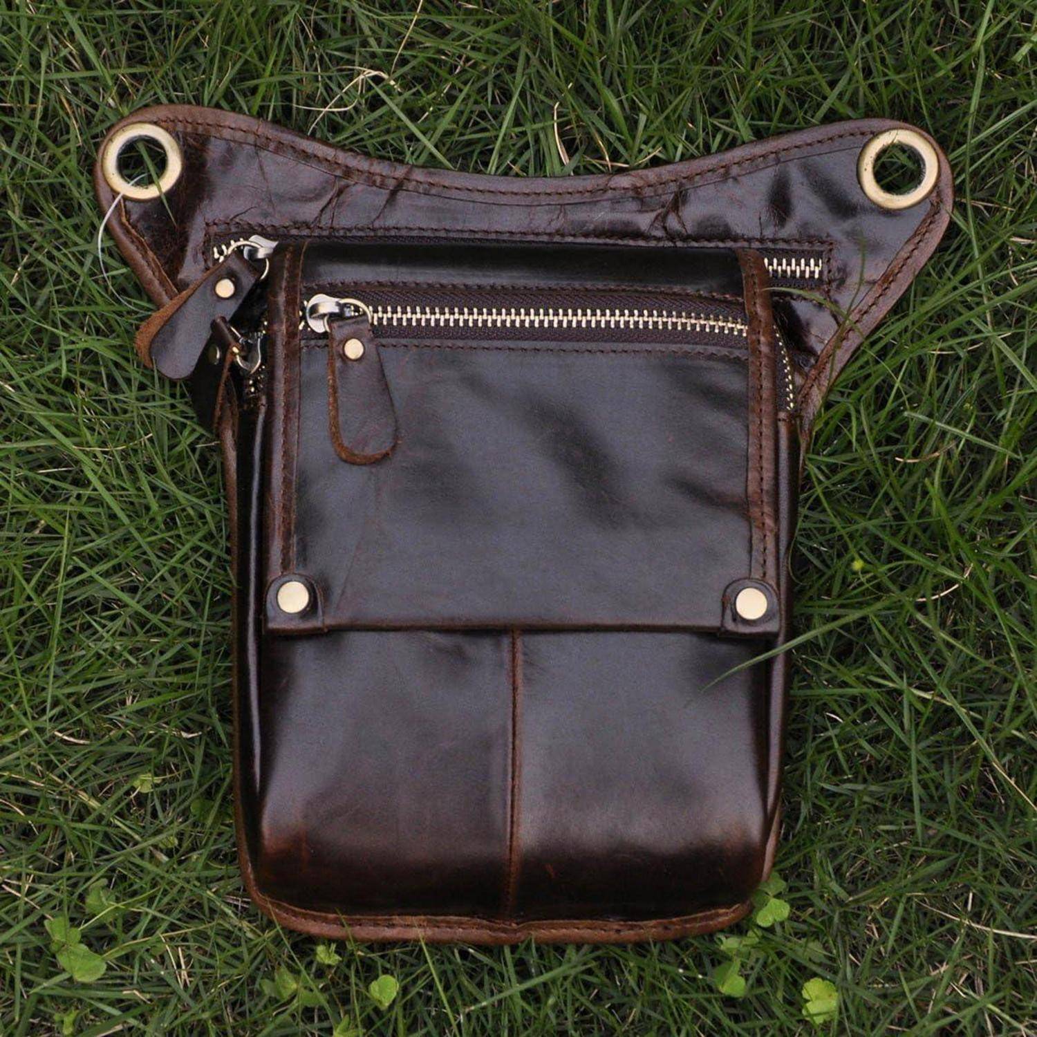 Braune Ledertasche zum Umhängen mit Klapptasche und Reißverschlüssen, flach auf Gras gelegt.