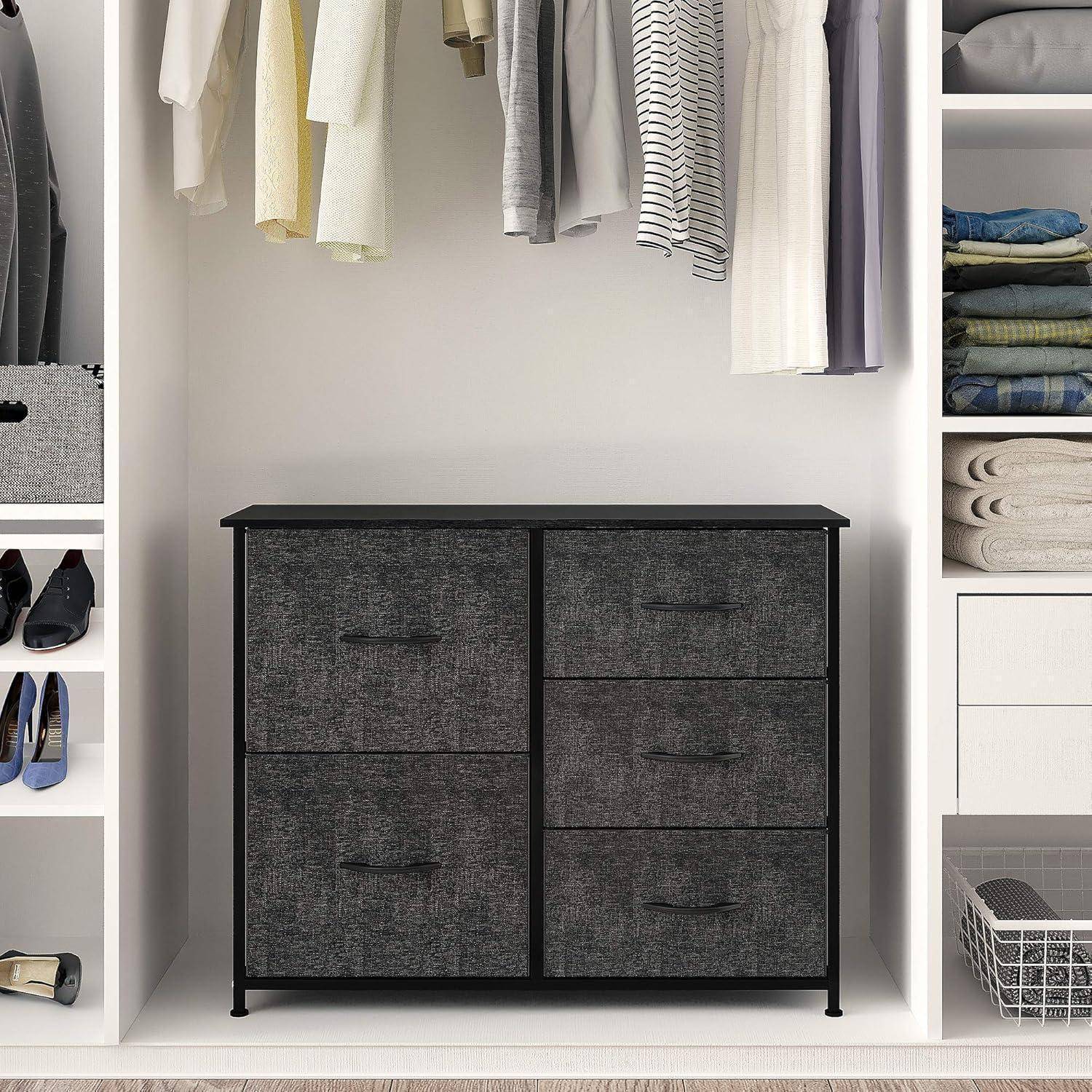 Abstellbereich im Kleiderschrank mit einer schwarzen zweitürigen Kommode, hängenden Kleidern oben und Regalen auf beiden Seiten mit gefalteten Kleidungsstücken und Schuhen.