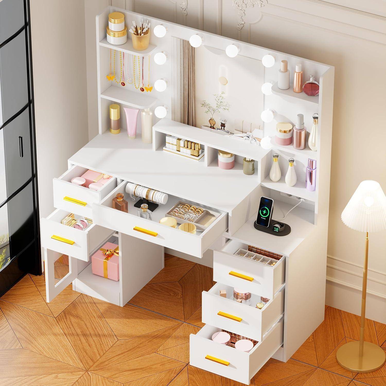 Weißer Frisiertisch mit Spiegel und beleuchteten Glühbirnen, offene Schubladen, Regale mit Kosmetik und Schmuck, plus eine Stehlampe in einem hellen Raum.