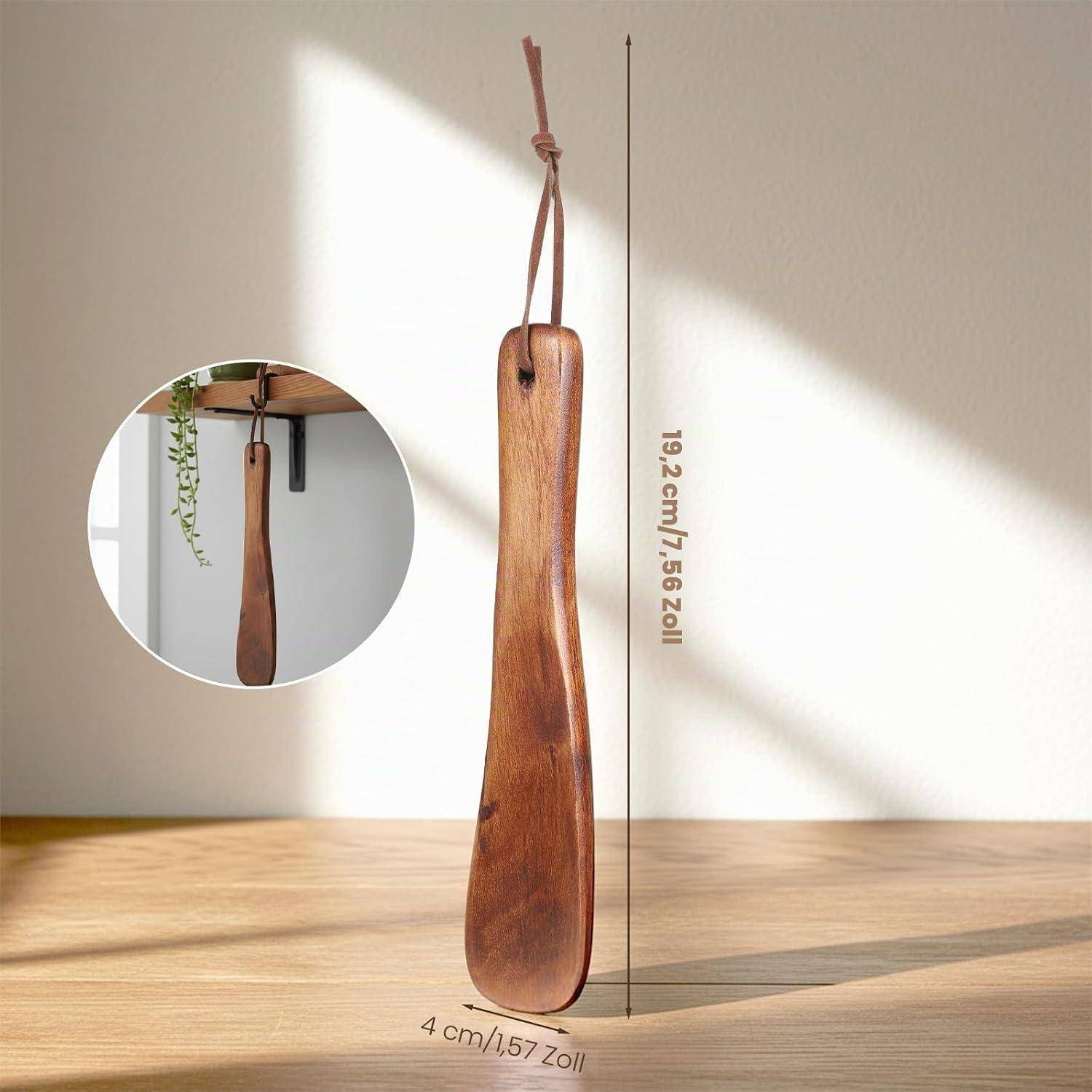 Holzschuhhorn mit Lederriemen, vertikal an einer Wand hängend, mit Größenangaben dargestellt: 19,2 cm lang und 4 cm breit.