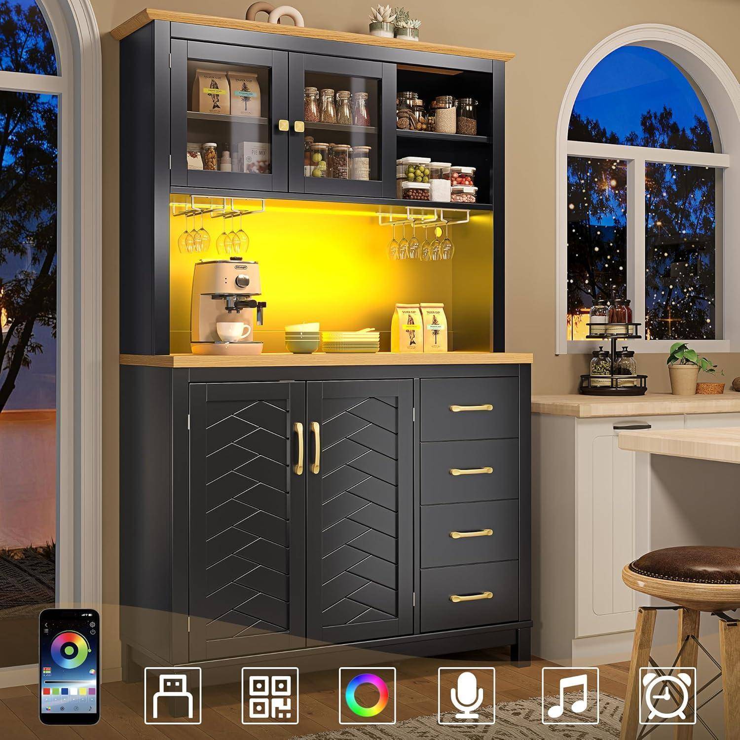 Dunkelgrauer Kücheneschrank mit Glastüren, beleuchteter gelber Rückwand, Regale, Kaffeemaschine und Tassen, neben einem Fenster und einer Arbeitsplatte in der Dämmerung.