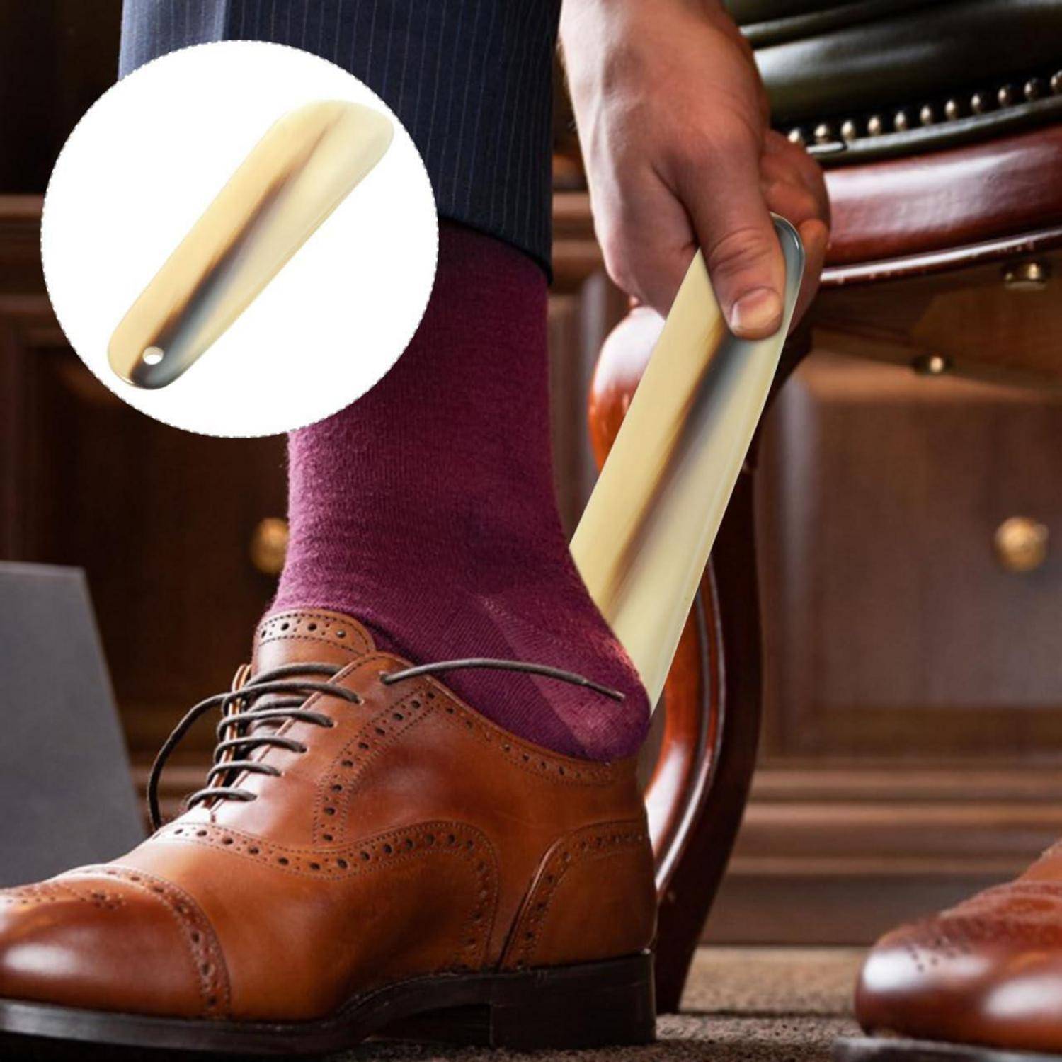 Eine Person benutzt einen Schuhanzieher, um einen braunen Lederschuh über einer violetten Socke auszuziehen.