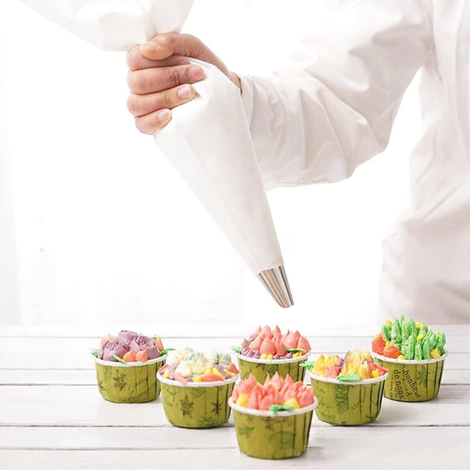 Konditor spritz Glasur mit einem Spritzbeutel auf kleine bunte Cupcakes in Papierkapseln auf einem weißen Tisch.