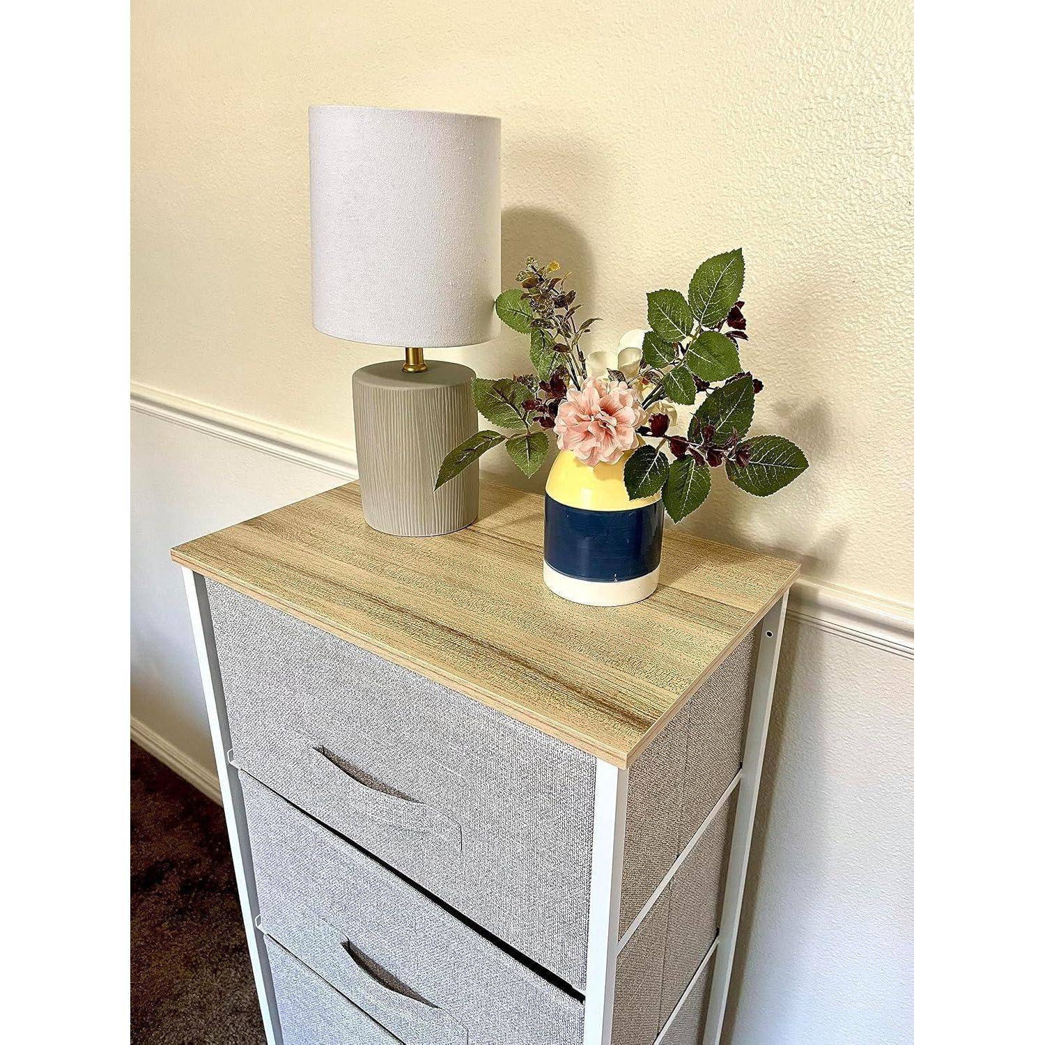 Kleine Holzkommode mit zwei Schubladen, darauf eine weiße Tischlampe und eine Blumenvase vor einer hellen Wand.