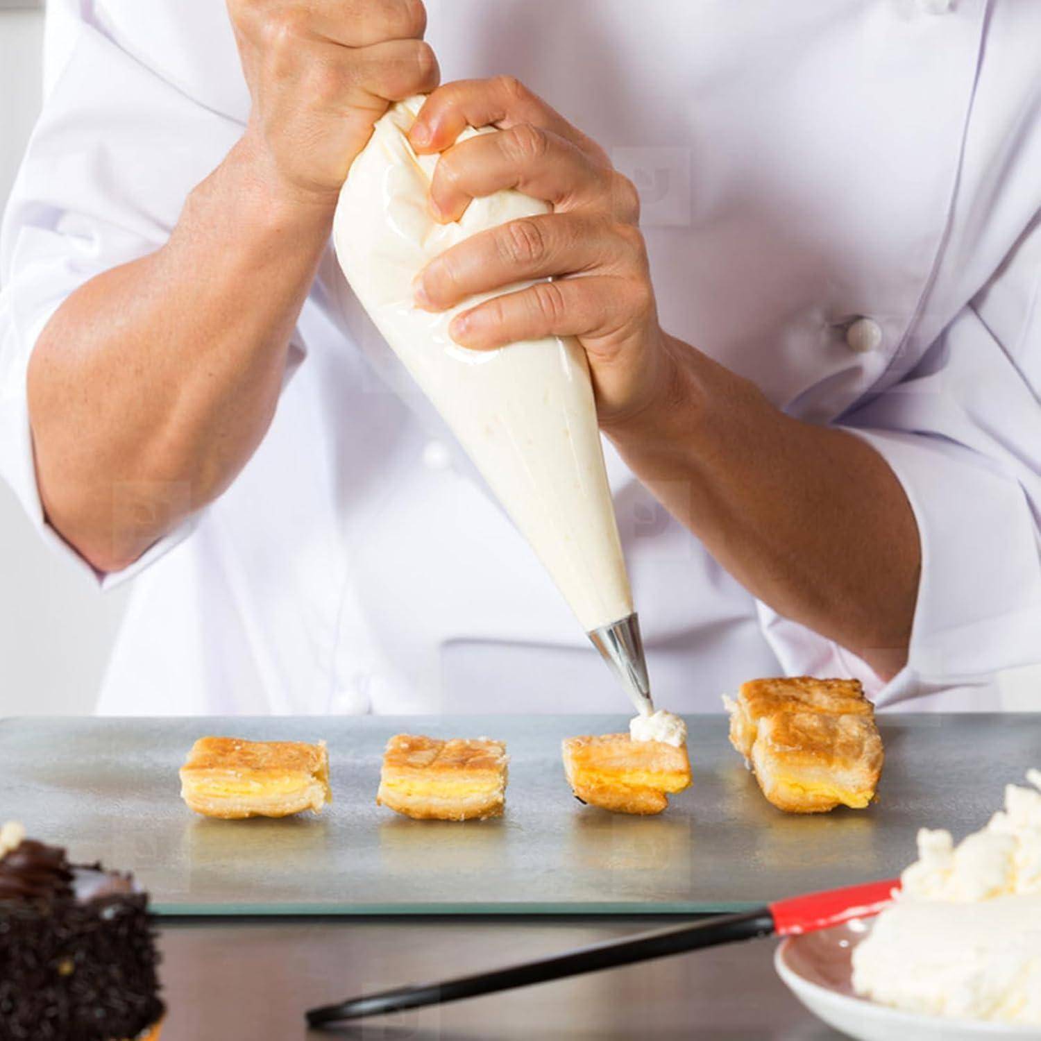 Ein Chef spritzt Sahne auf kleine Gebäckstücke auf einem Tablett und dekoriert Desserts in einer Küche.