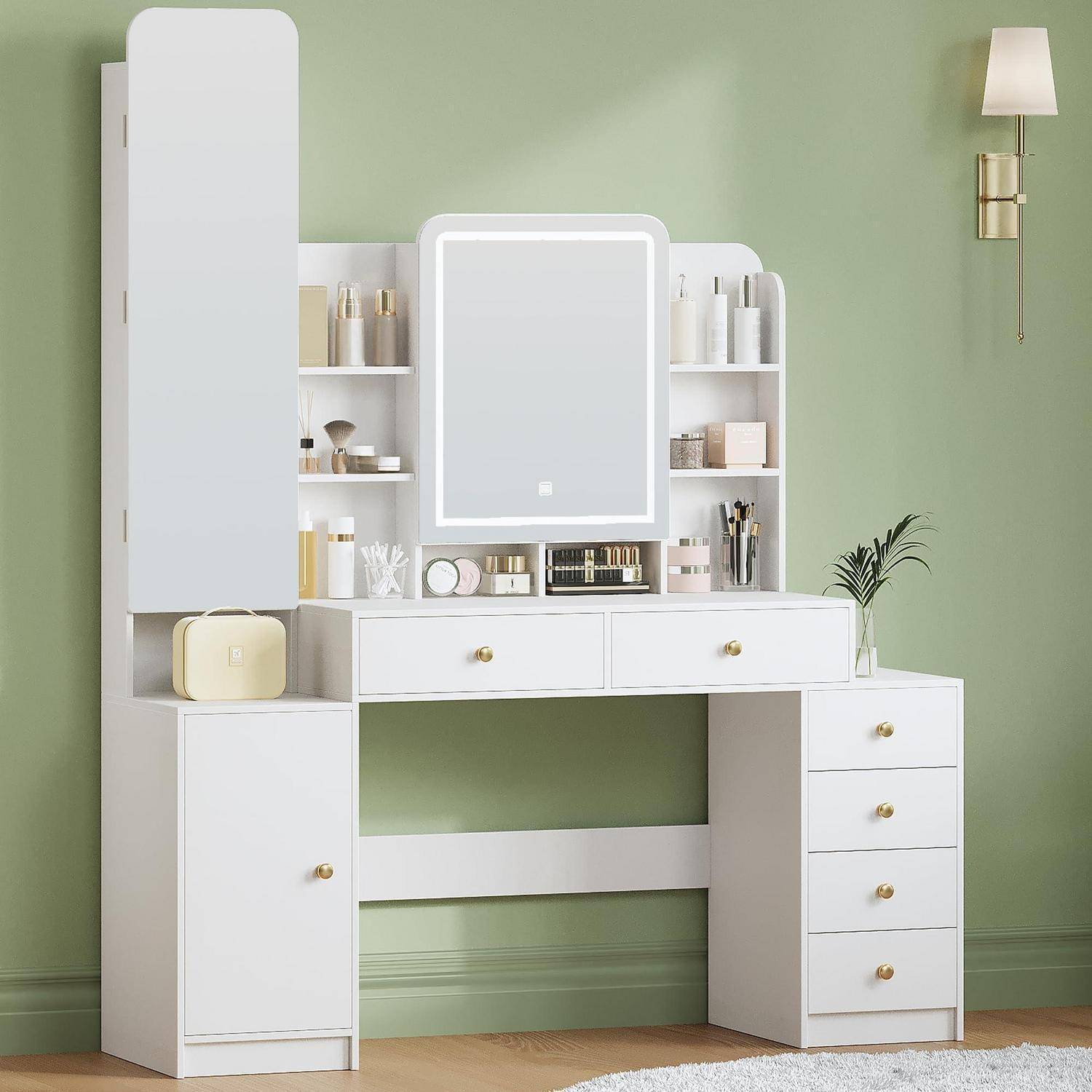 Weißer Schminkentisch mit Spiegel, Regalen und Schubladen an einer grünen Wand, zeigt organisierte Makeup-Aufbewahrung und eine Wandleuchte.