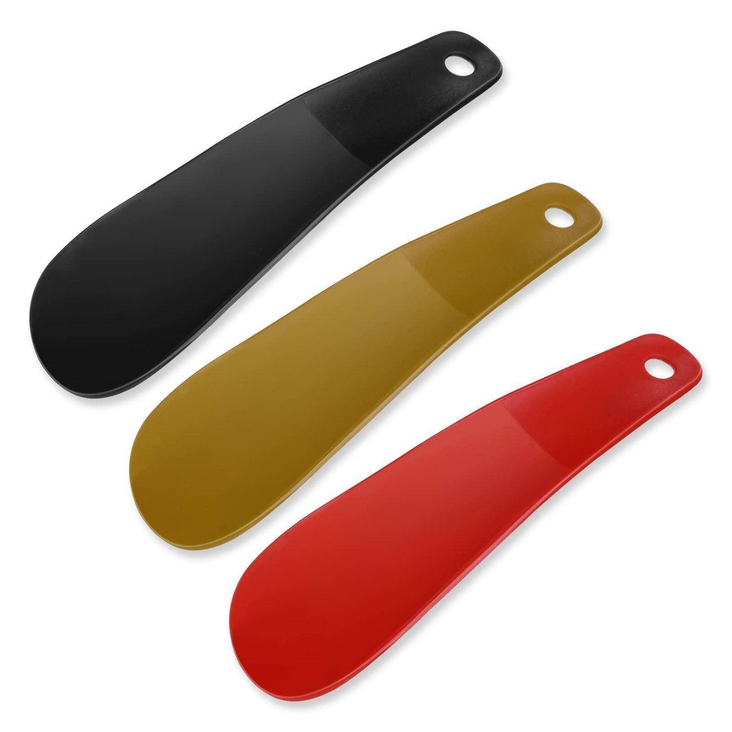 Drei farbige Schuhanzieher – schwarz, gold und rot – diagonal auf weißem Hintergrund angeordnet.