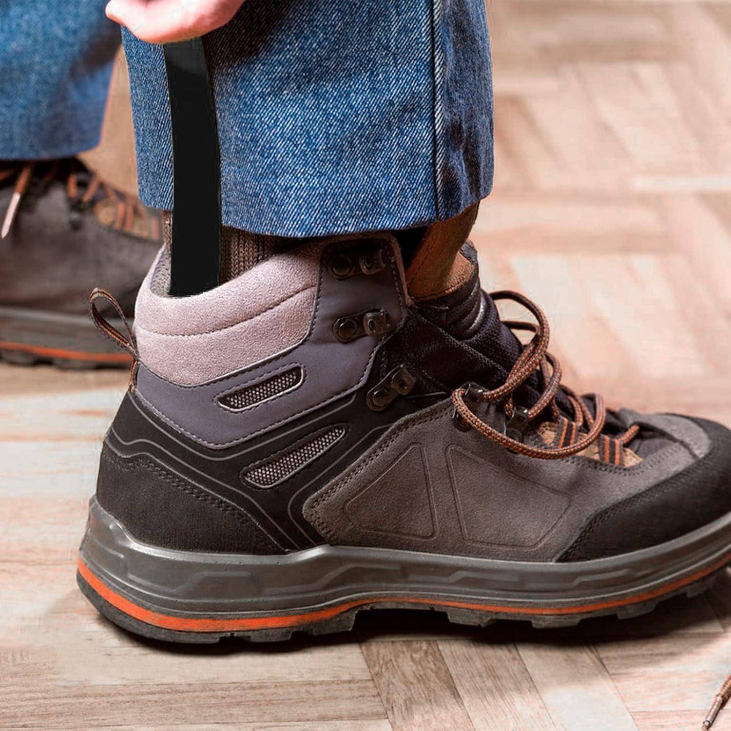 Nahaufnahme einer Person, die einen braunen Wanderstiefel auf einem Holzboden trägt, mit über dem Knöchel umgeschlagenen Jeans und einem schwarzen Riemen oder Etikett in der Nähe der Ferse.