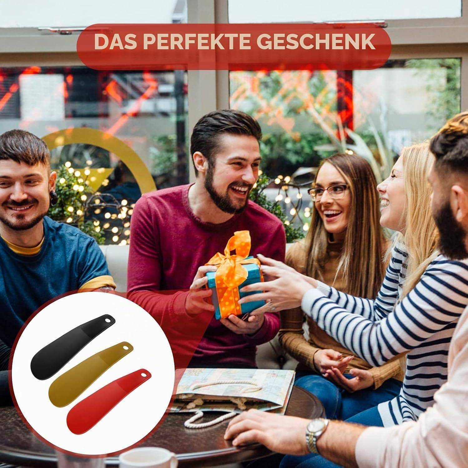 Freunde lächeln, während ein Mann ein kleines verpacktes Geschenk überreicht; deutscher Text sagt „DAS PERFEKTE GESCHENK