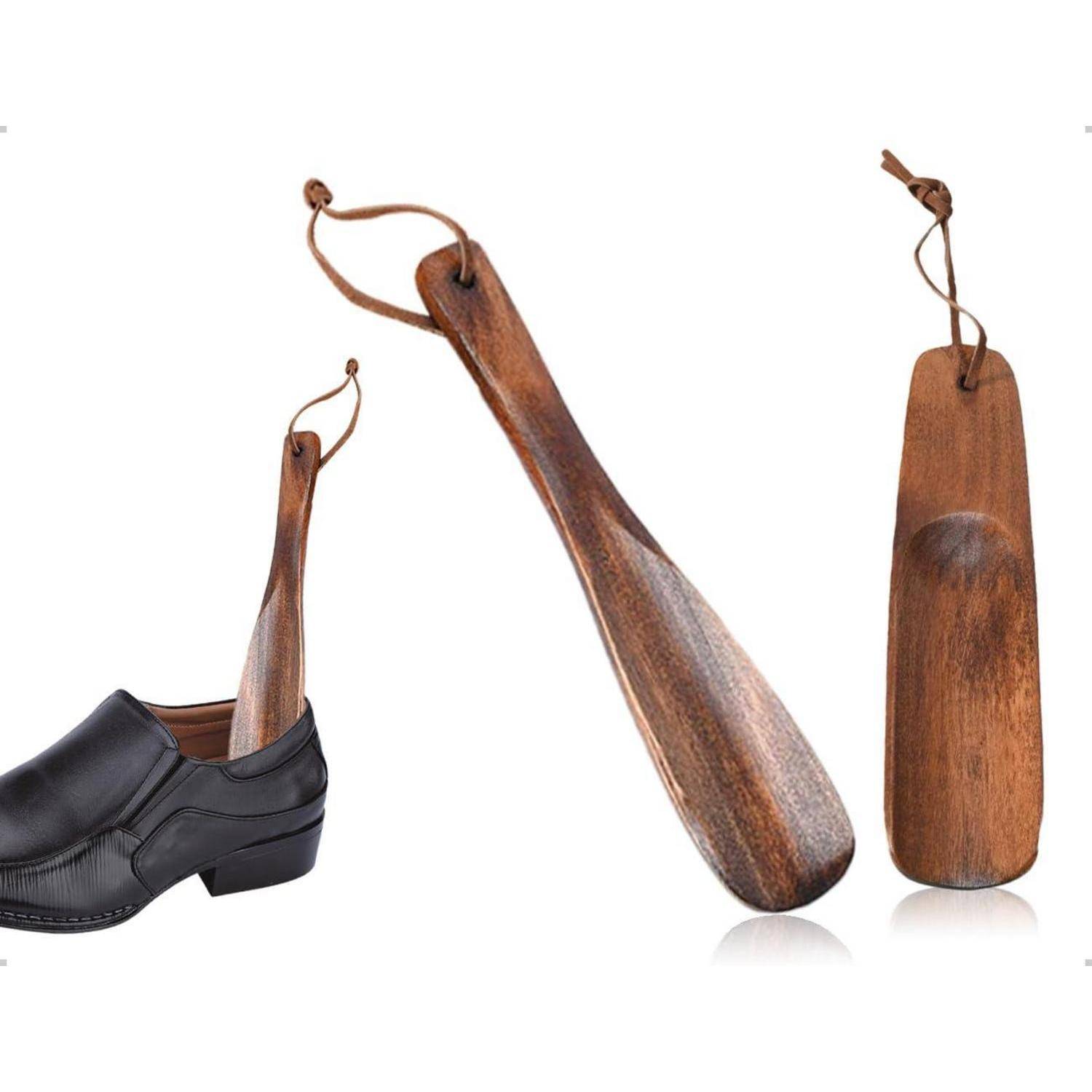 Drei Holzschuhlöffel unterschiedlicher Länge, einer in einen schwarzen Herrenschuh eingesteckt, auf weißem Hintergrund.