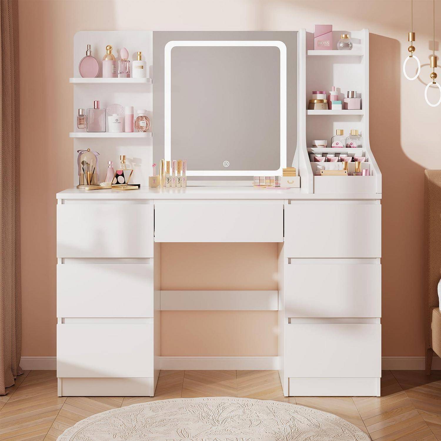 Weißer Frisiertisch mit Spiegel und Regalen, ordentlich arrangiert mit Kosmetik und Parfüm in einem zartrosa Schlafzimmer.