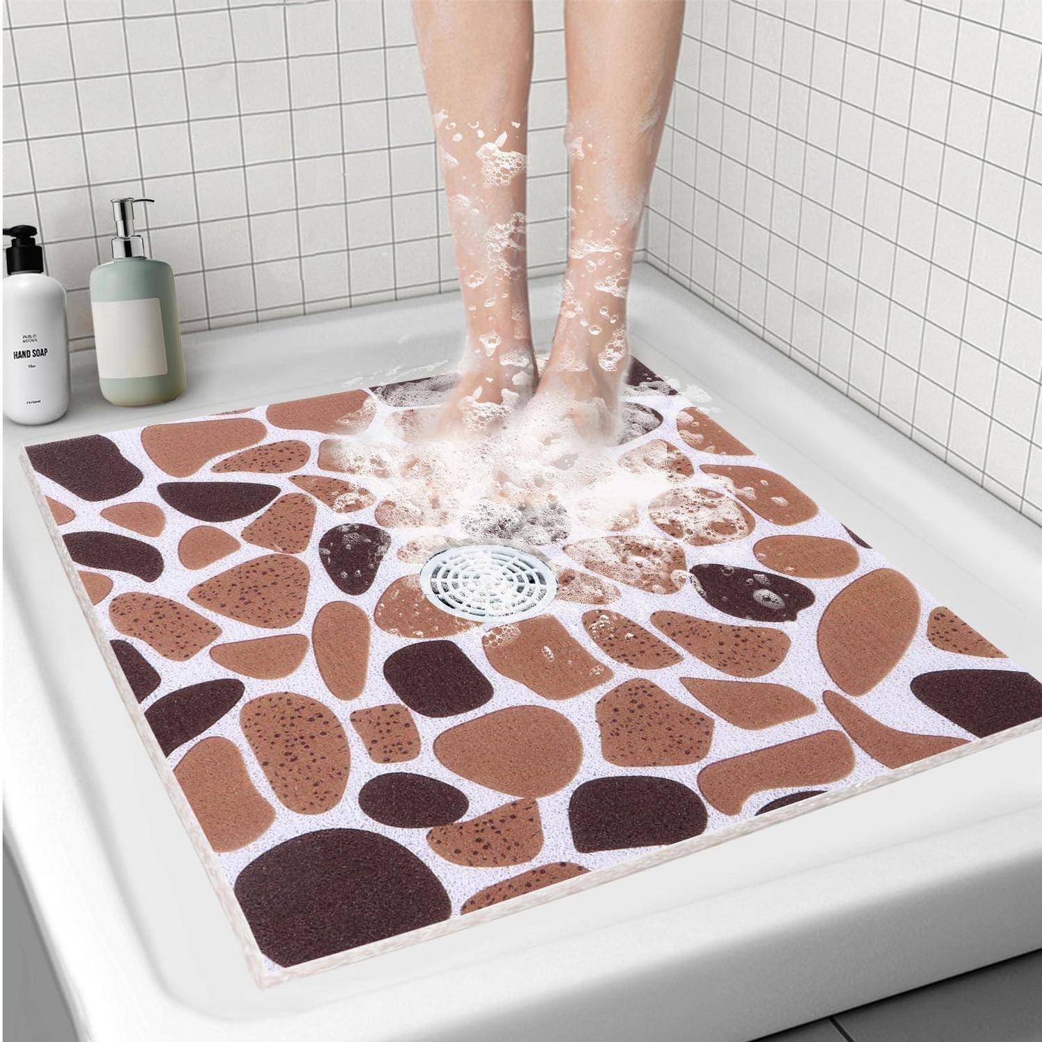 Eine Person steht in einer Dusche und wäscht sich die Füße auf einer Badmatte mit Steinmuster über dem Ablauf, mit Seifenschaum um die Knöchel.