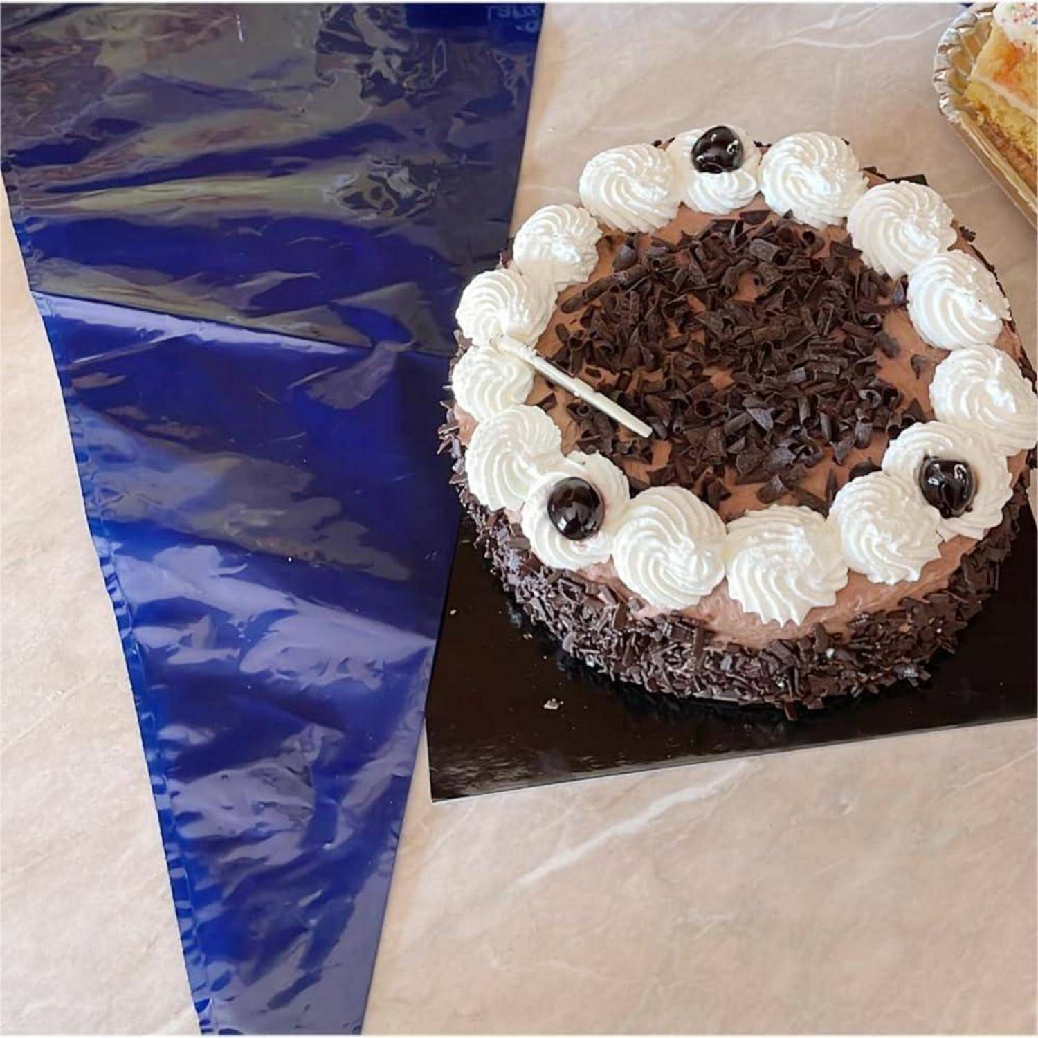 Schokoladenkuchen mit Schlagsahnerosetten und Schokoladenkrümeln auf einem Tisch neben einem Spritzbeutel mit blauem Zuckerguss.