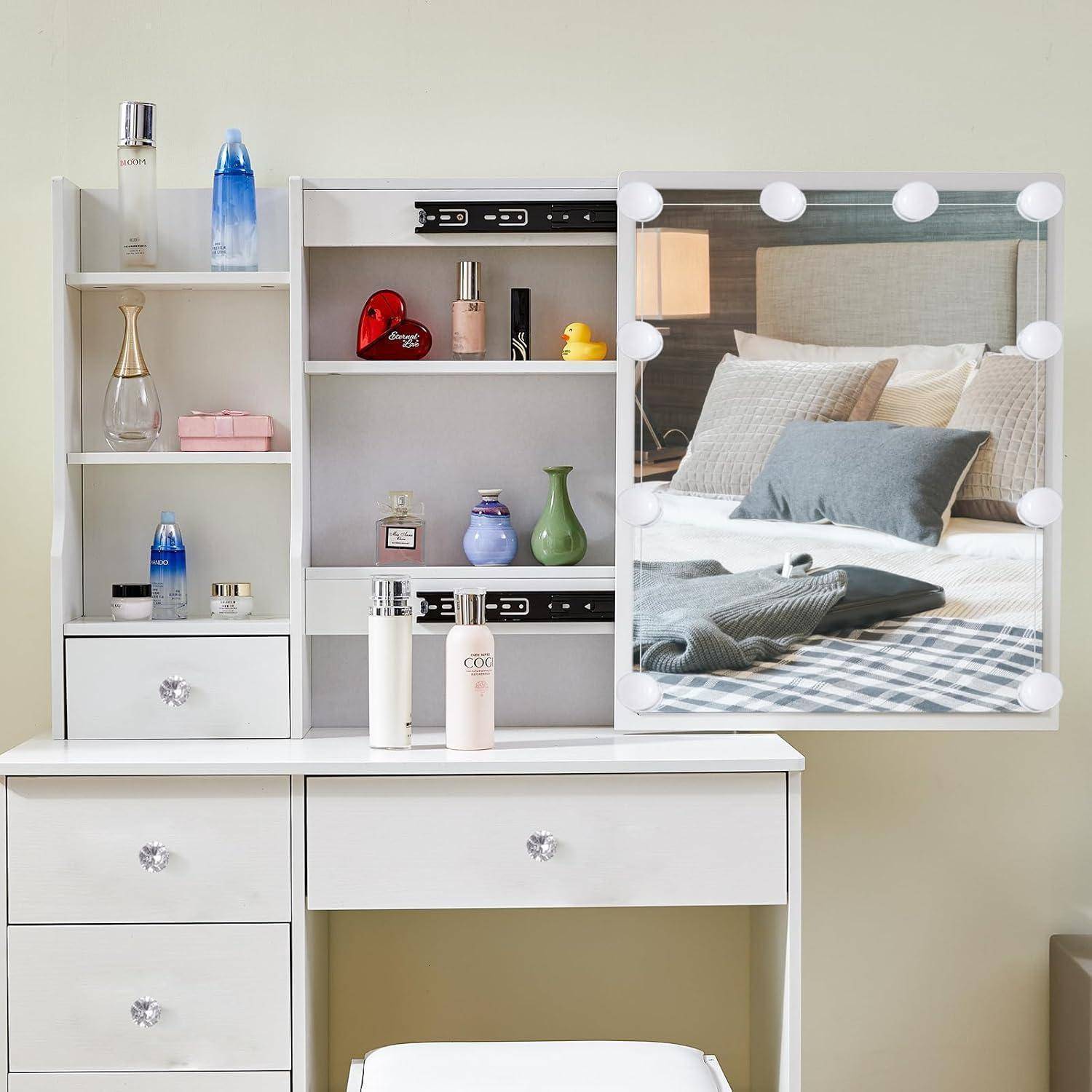Weißes Frisiertischset mit Spiegel, Schubladen und Regalen, die Kosmetik und Dekoration enthalten; der Spiegel spiegelt ein gemachtes Bett mit Kissen und einer Lampe wider.