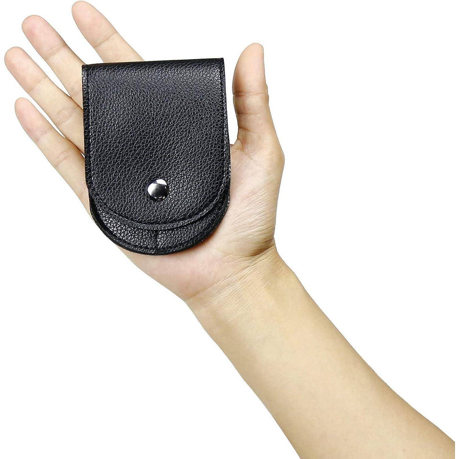 Eine Hand hält ein kleines schwarzes Ledertäschchen mit Druckknopfverschluss, gezeigt vor einem einfachen weißen Hintergrund.