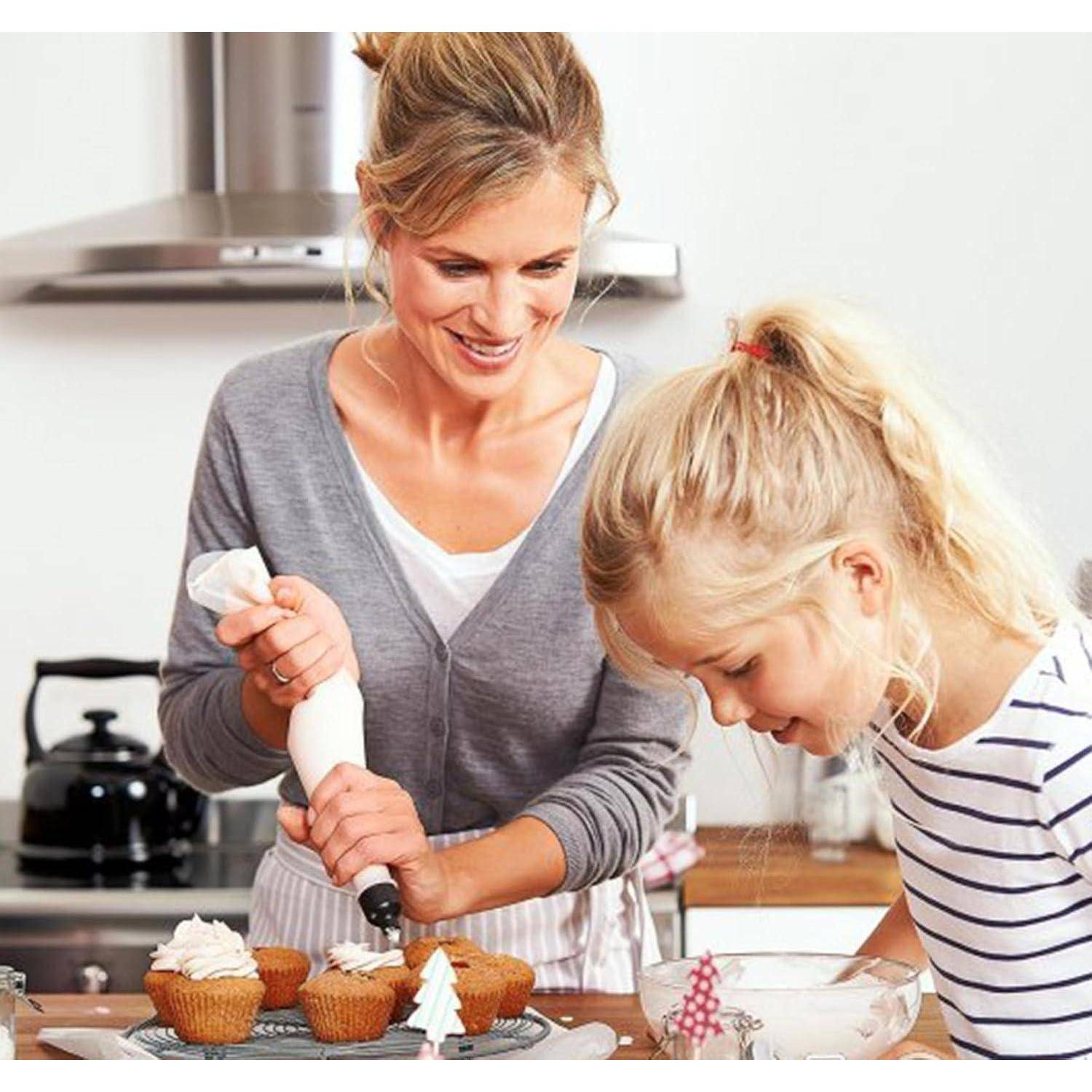 Mutter und Tochter dekorieren gemeinsam Cupcakes in einer Küche, mit Spritztüten, gebackenen Cupcakes und einer Rührschüssel auf der Arbeitsplatte.