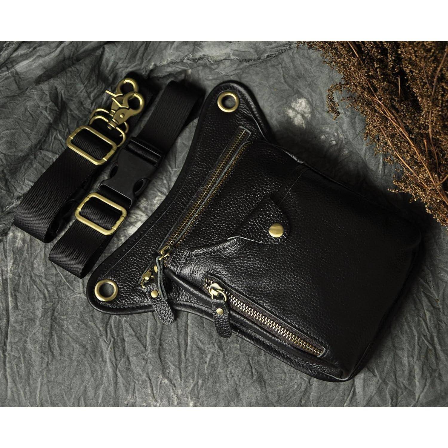 Schwarze Ledertasche zum Umhängen mit goldfarbenen Reißverschlüssen und Beschlägen, gezeigt mit einem breiten verstellbaren Riemen auf zerknittertem grauem Hintergrund.