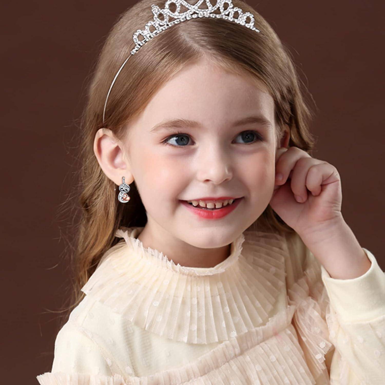 Junges Mädchen mit Diadem und Ohrringen, lächelnd in einem cremefarbenen Kleid vor einem einfachen braunen Hintergrund.