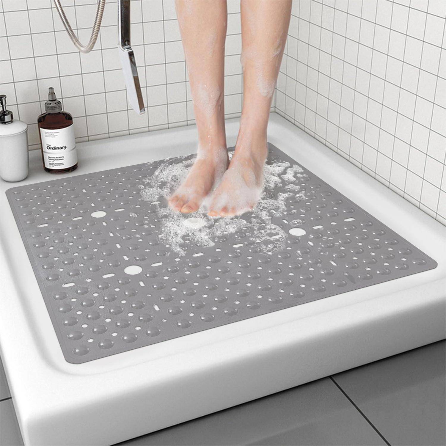 Person steht unter der Dusche mit Füßen auf einer grauen rutschfesten Matte, Wasser spritzt um sie herum.