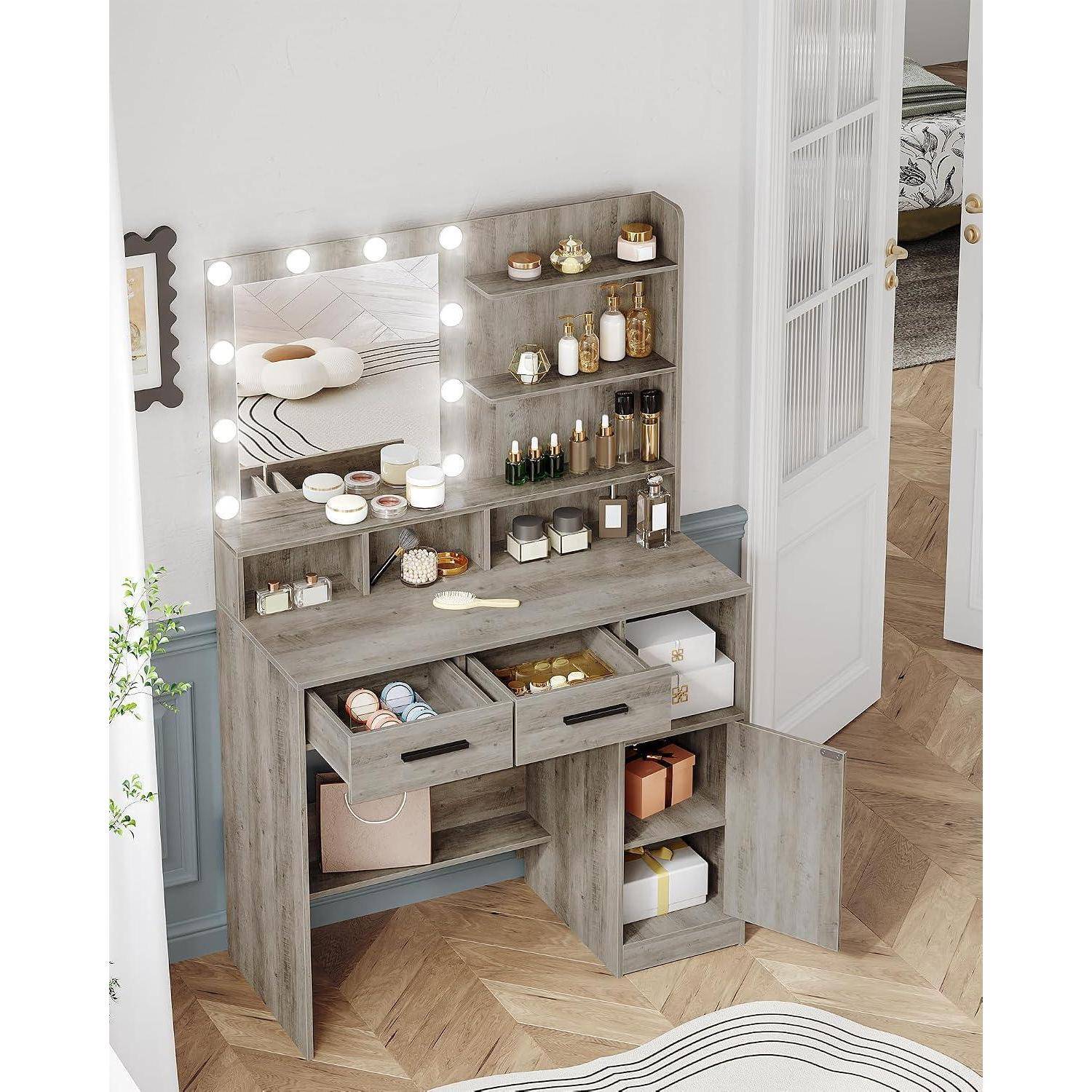 Grauer Schminkschrank mit beleuchtbarem Spiegel, Regale mit Kosmetikprodukten und offene Schubladen, die organisierte Beauty-Artikel in einem hellen Raum zeigen.
