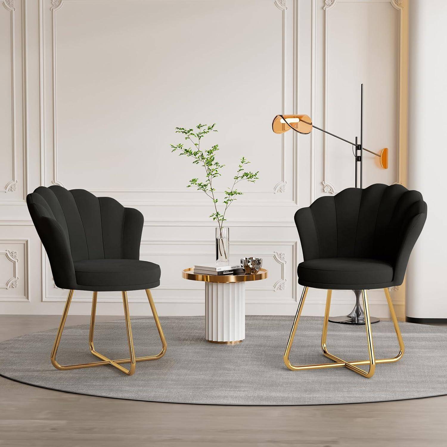 Zwei schwarze Schalenstühle mit goldenen Beinen flankieren einen kleinen runden Tisch und eine Vase in einem modernen, minimalistischen Wohnbereich.