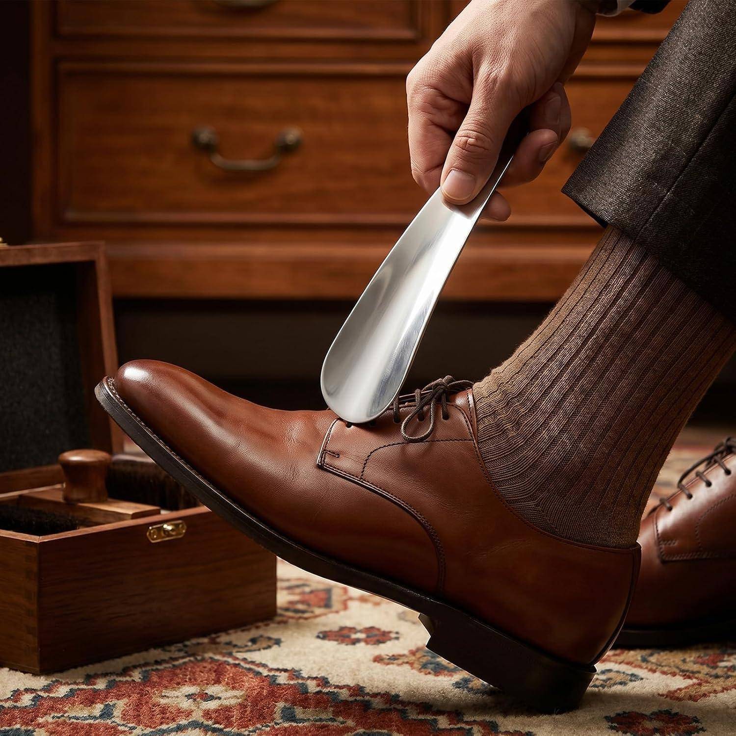 Eine Hand benutzt einen Metallschuhlöffel, um einen braunen Lederschuh auf einen Fuß mit braunen gerippten Socken zu gleiten.
