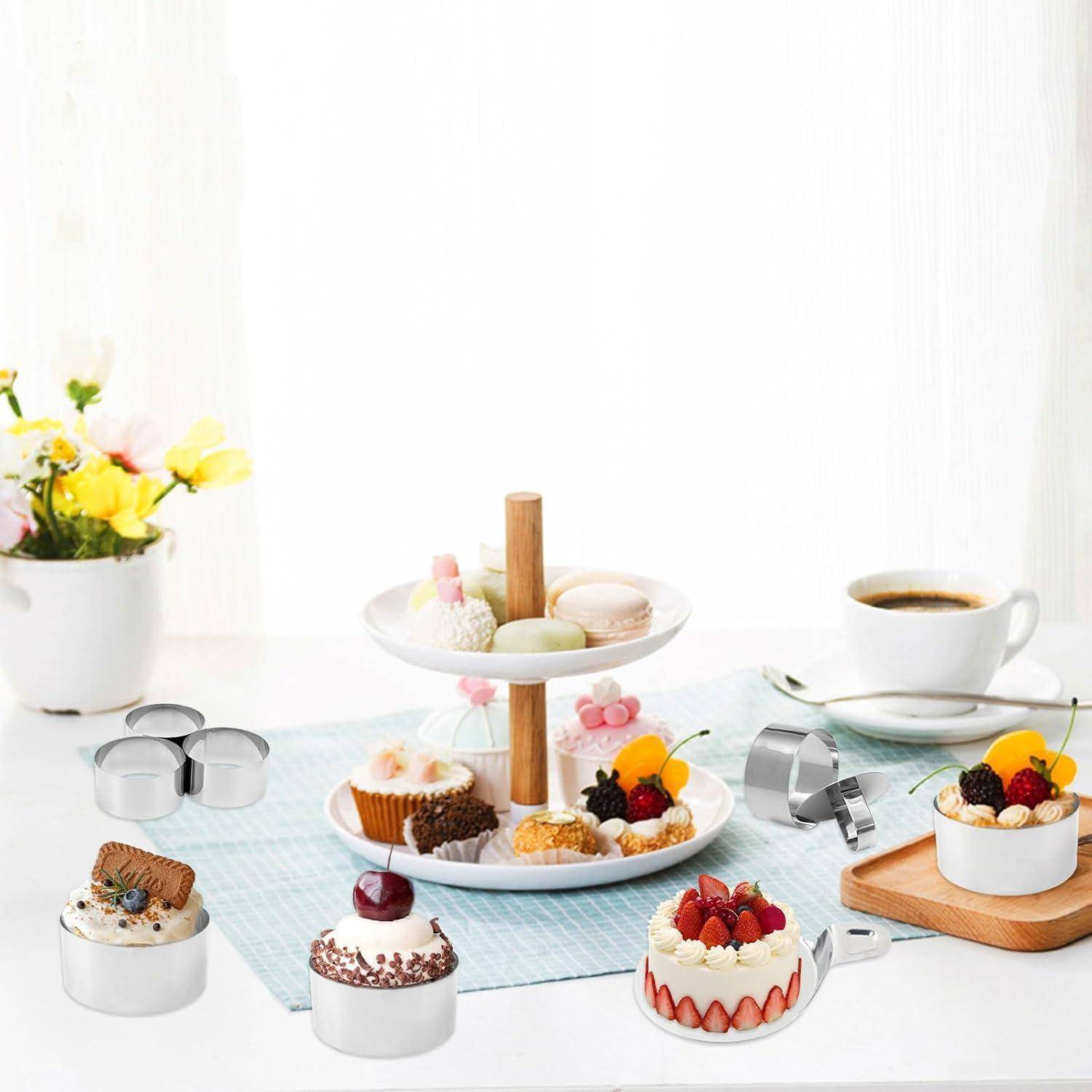 Elegante Dessertpräsentation mit assortiertem Gebäck und fruchtverziertem Kuchen auf Ständern und Tellern, daneben Kaffeetassen und eine Vase mit Blumen auf einem weißen Tisch.