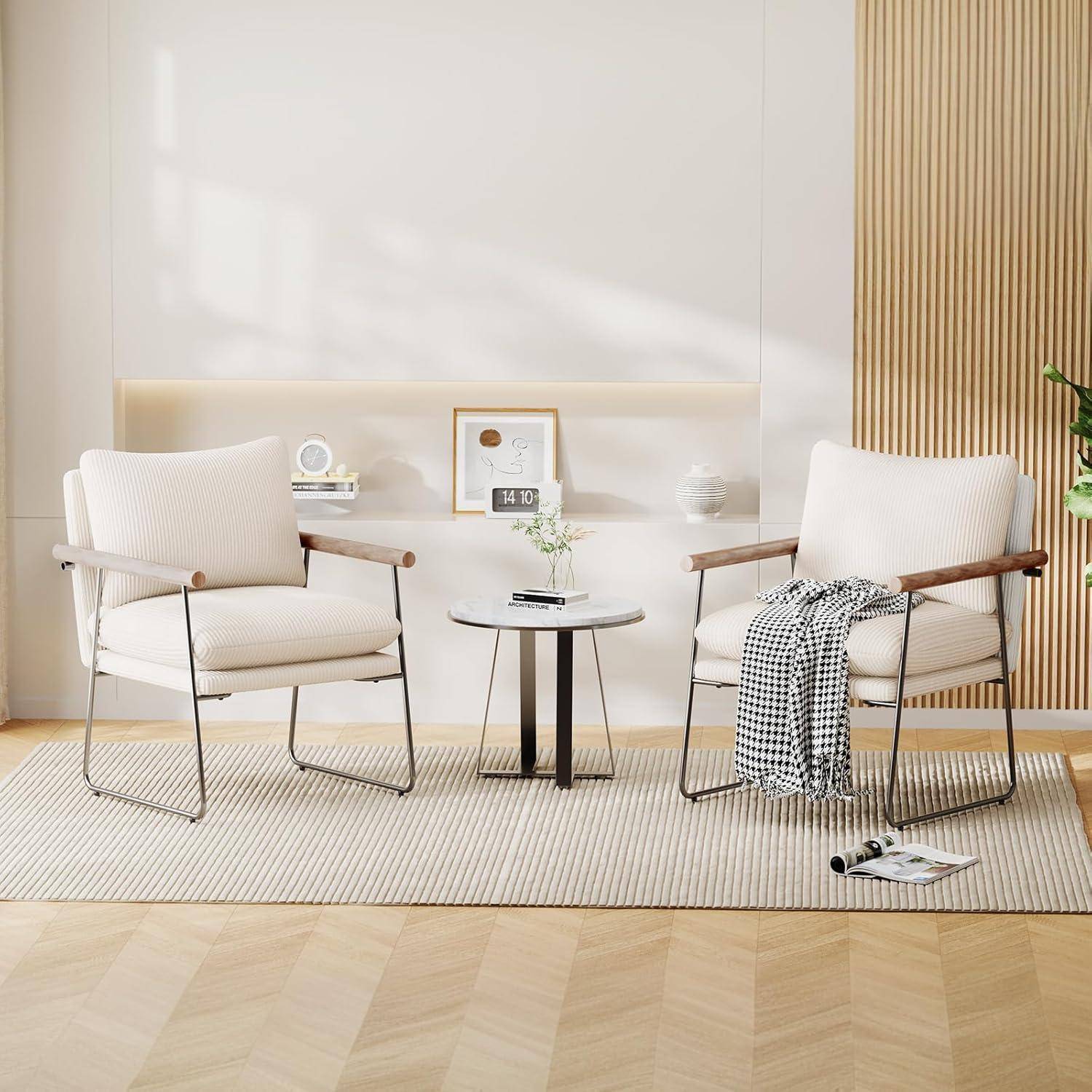 Zwei cremefarbene Sessel flankieren einen kleinen runden Tisch in einem minimalistischen Wohnzimmer, wobei einer der Sessel mit einem Überwurf drapiert ist und helle Holzakzente das Ambiente prägen.