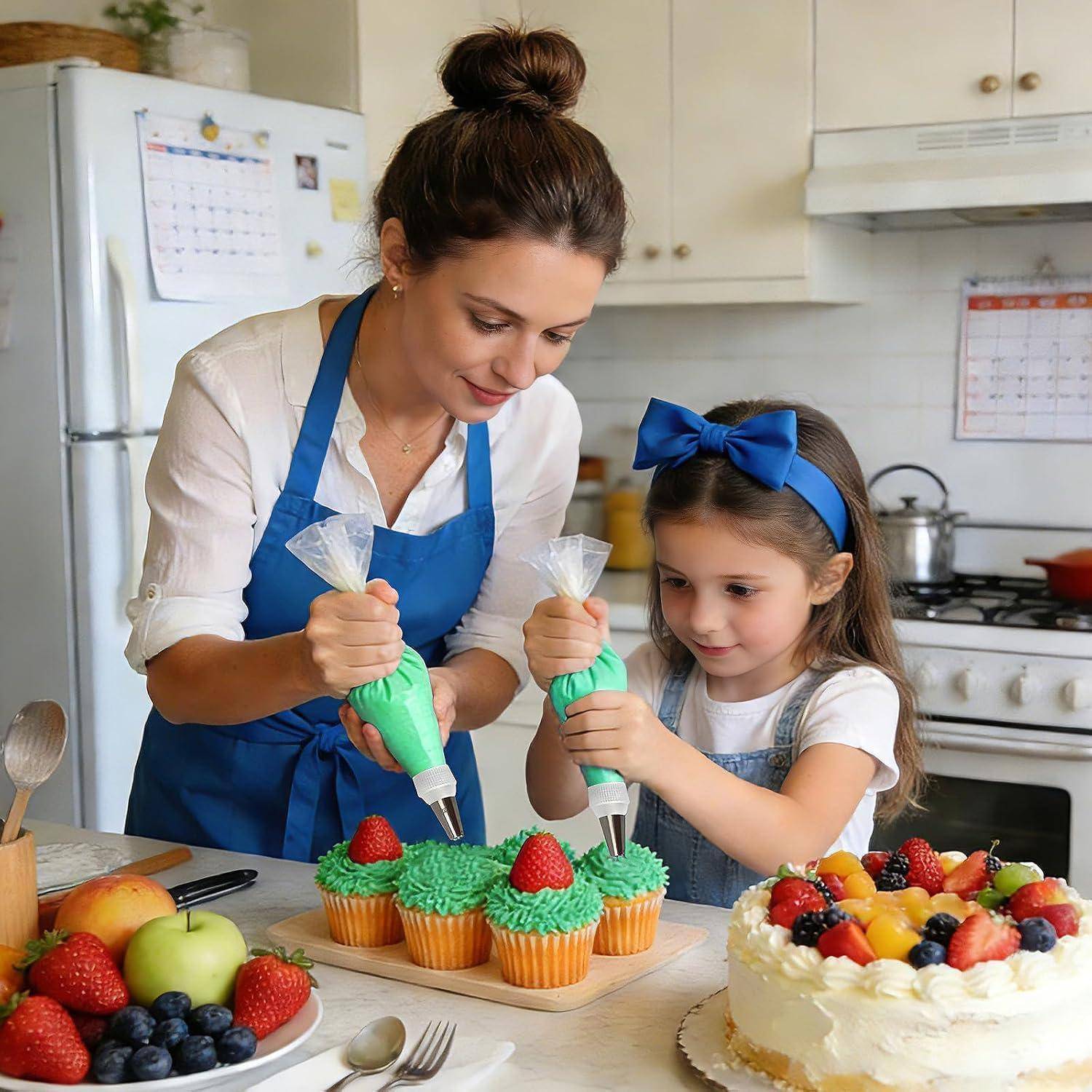 Frau und junges Mädchen dekorieren zusammen Cupcakes in einer Küche, spritzen grüne Glasur auf und fügen Erdbeeren neben einem obstbedeckten Kuchen hinzu.