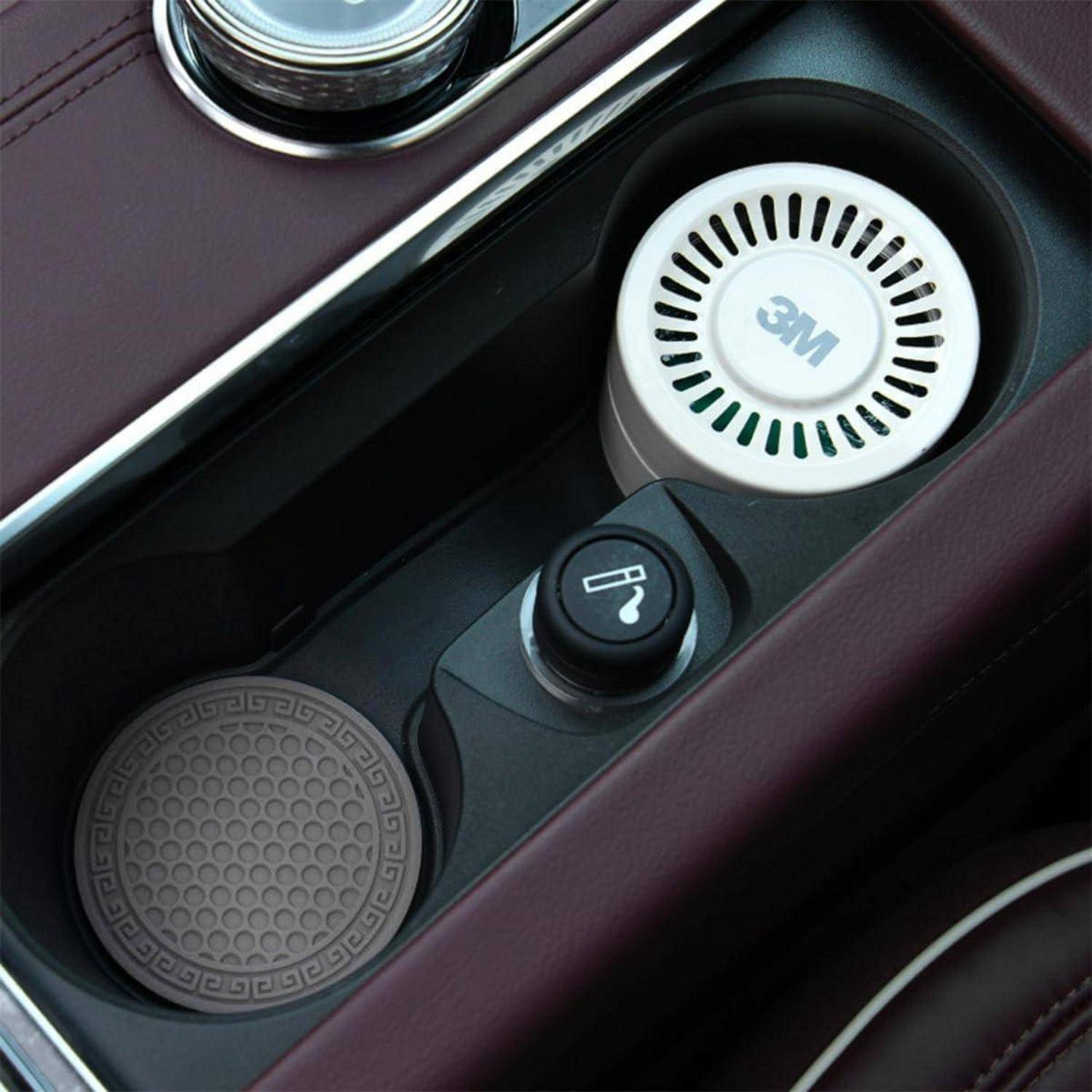 Mittelkonsole des Autos mit einem 3M-Lufterfrischer, Getränkehalter und Stromanschluss-Taste in einer dunklen Lederausstattung.