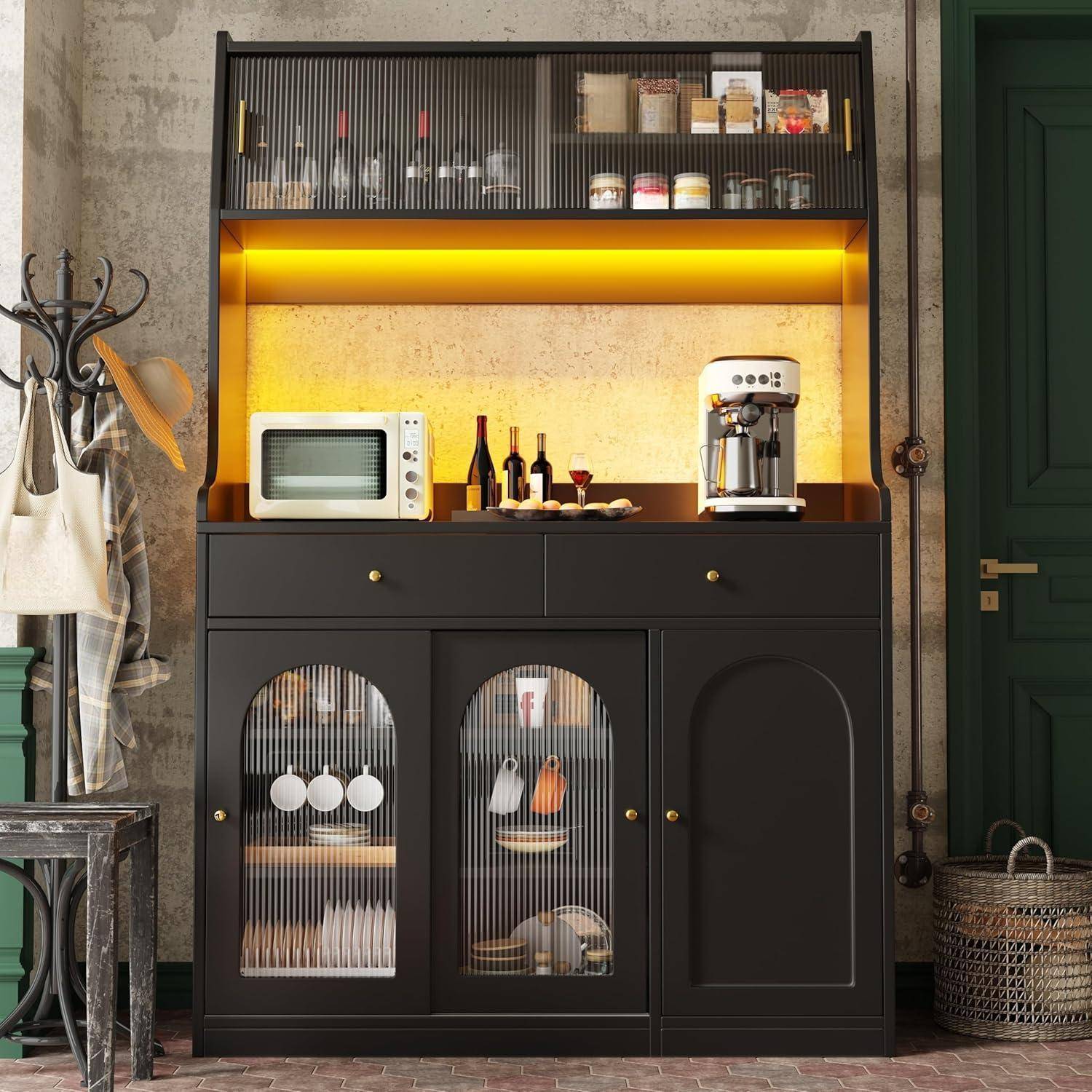 Ein schwarzer Küchenschrank mit Glastüren und Regalen enthält eine Mikrowelle, Flaschen, Geschirr und eine Kaffeemaschine, beleuchtet durch warme Unterbodenleuchten.