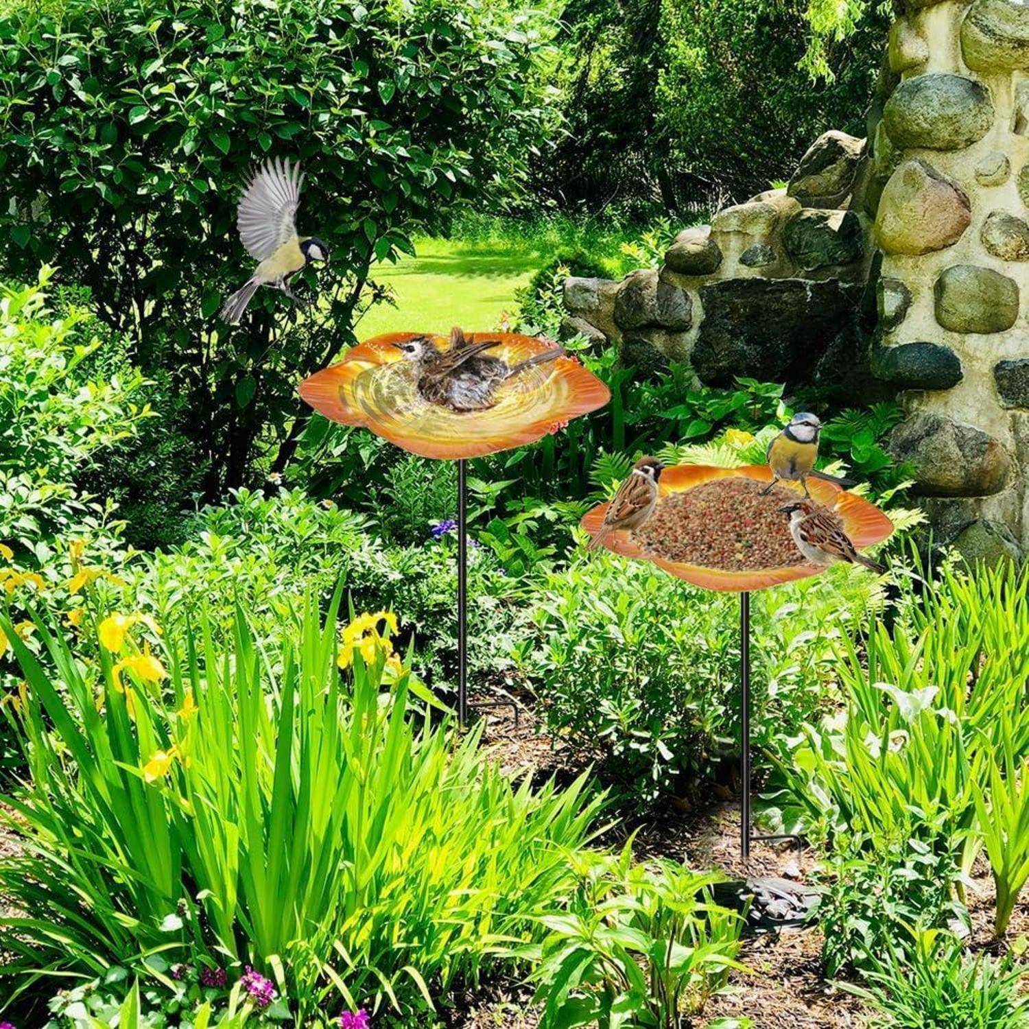 Gartenszene mit zwei Vogelfutterhäuschen, in denen kleine Vögel sitzen, umgeben von üppigem Grün neben einer Steinstruktur.