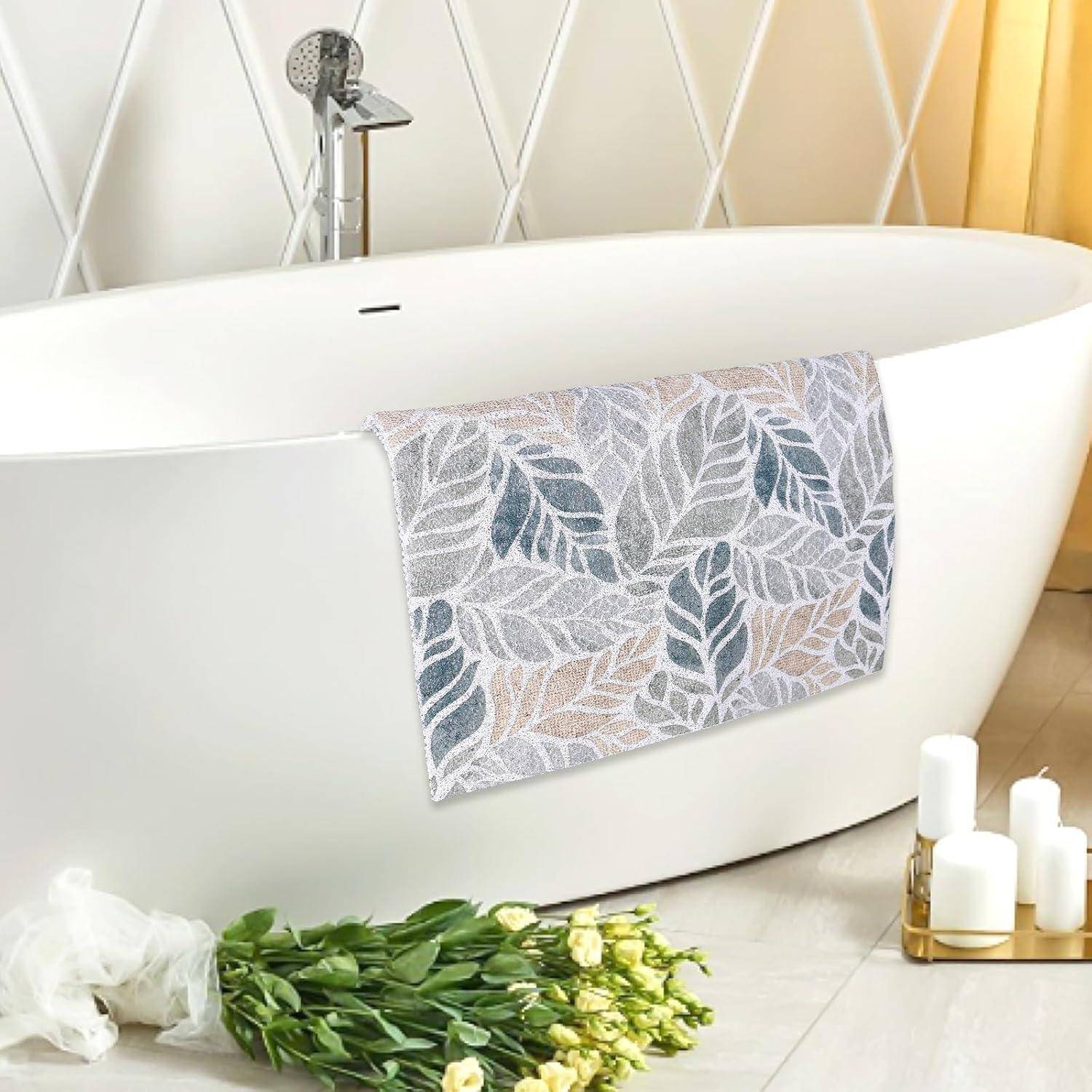 Freistehende weiße Badewanne mit Handtuch mit Blattmuster, Blumen auf dem Boden und Kerzen in der Nähe in einem hellen Badezimmer.