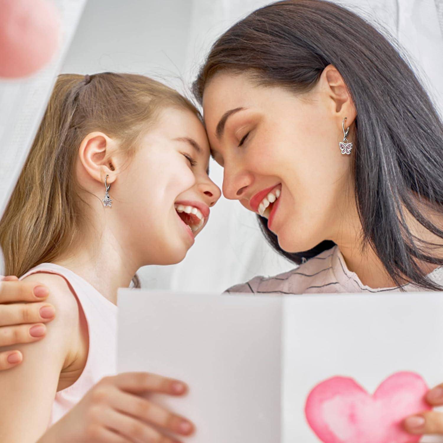 Mutter und kleine Tochter lächeln mit Stirnen, die sich berühren, während sie eine offene Karte mit einem rosa Herzen halten, was eine liebevolle Grußbotschaft oder Muttertagsnachricht andeutet.