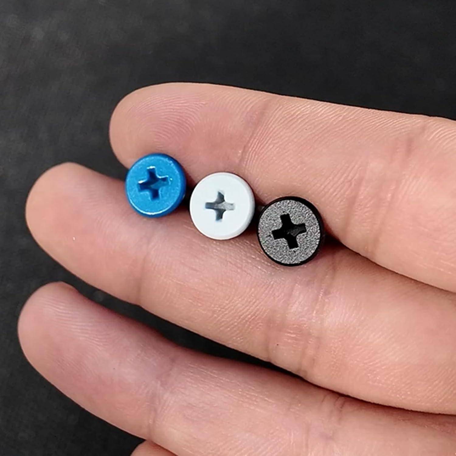 Drei kleine runde schraubenähnliche Befestigungselemente in Blau, Weiß und Schwarz ruhen auf den Fingern einer Person.