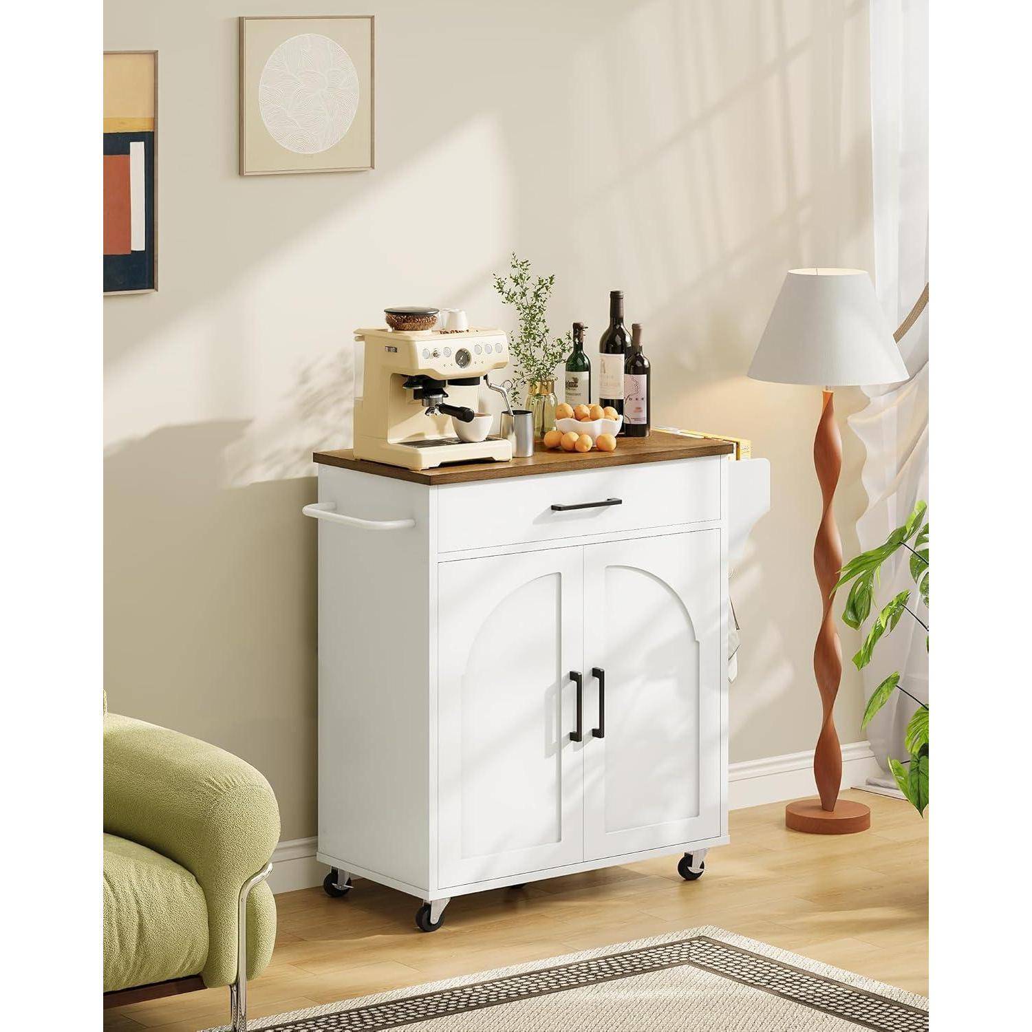 Weißer Küchenwagen mit Holzplatte, Espressomaschine, Flaschen und Obst neben einer Stehleuchte in einem hellen Wohnzimmer.
