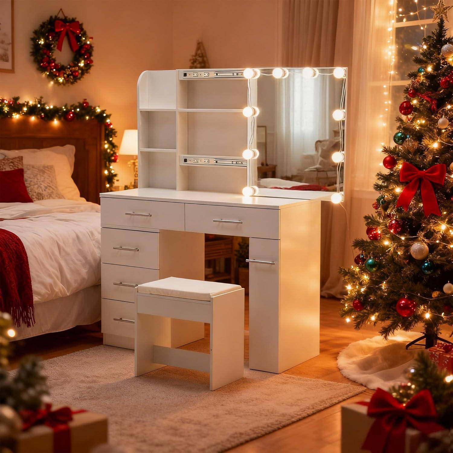 Weißer Frisiertisch mit beleuchtetem Spiegel und Hocker in einem warm dekorierten Weihnachtszimmer neben einem Bett und beleuchtetem Baum.