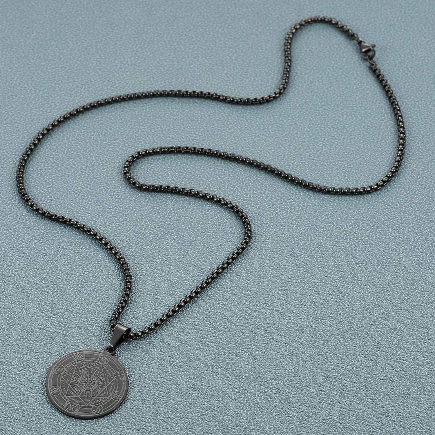 Schwarze Kettenkette mit rundem graviertem Anhänger auf hellgrauem Hintergrund.