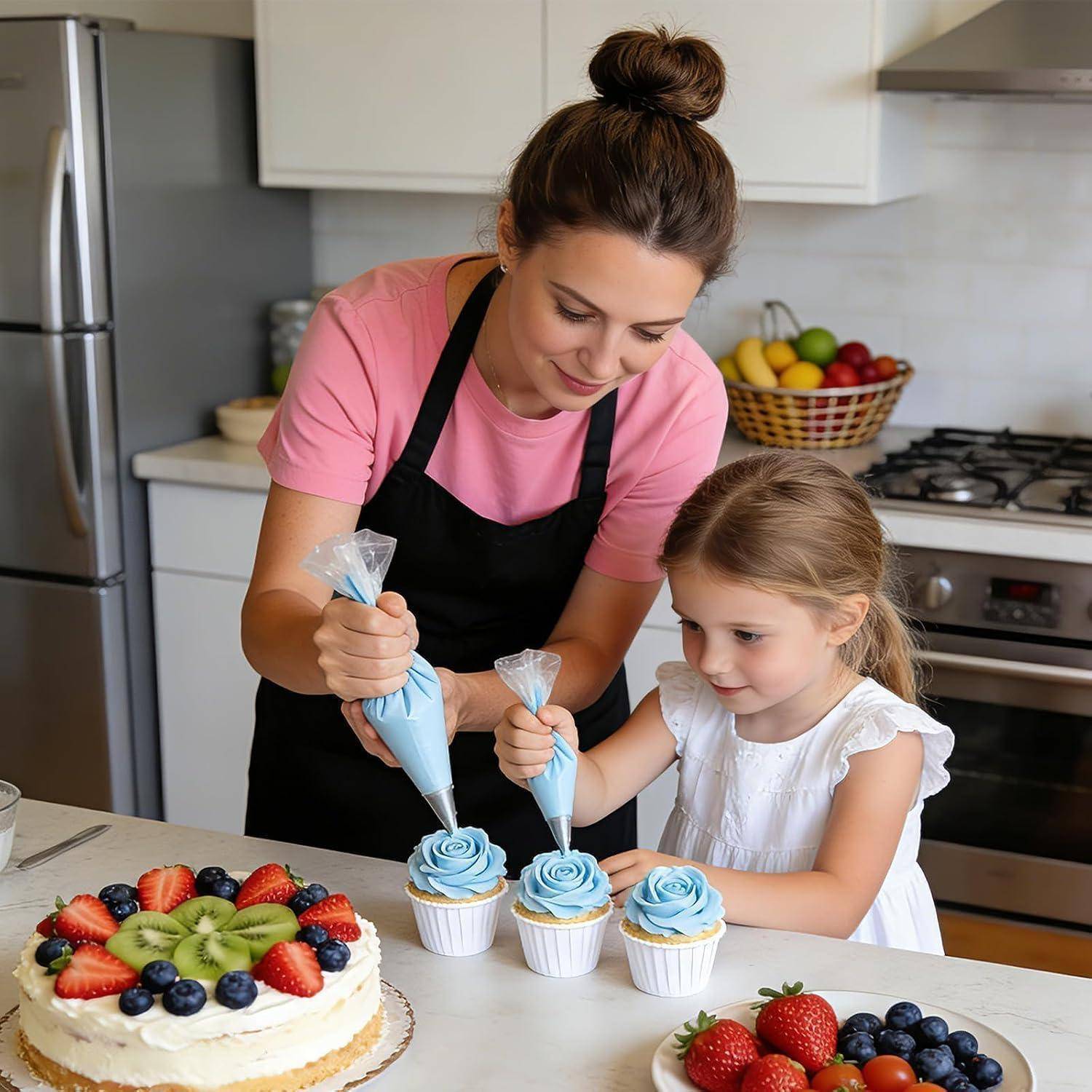 Frau und junges Mädchen, die Cupcakes mit blauem Zuckerguss in einer Küche dekorieren, mit fruchtbedeckten Kuchen und einer Schüssel mit Obst in der Nähe.