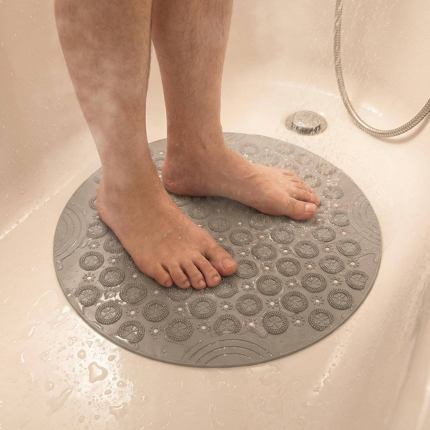 Nackte Füße stehen auf einer grauen, runden Duschvorlage in einer Badewanne oder Dusche.