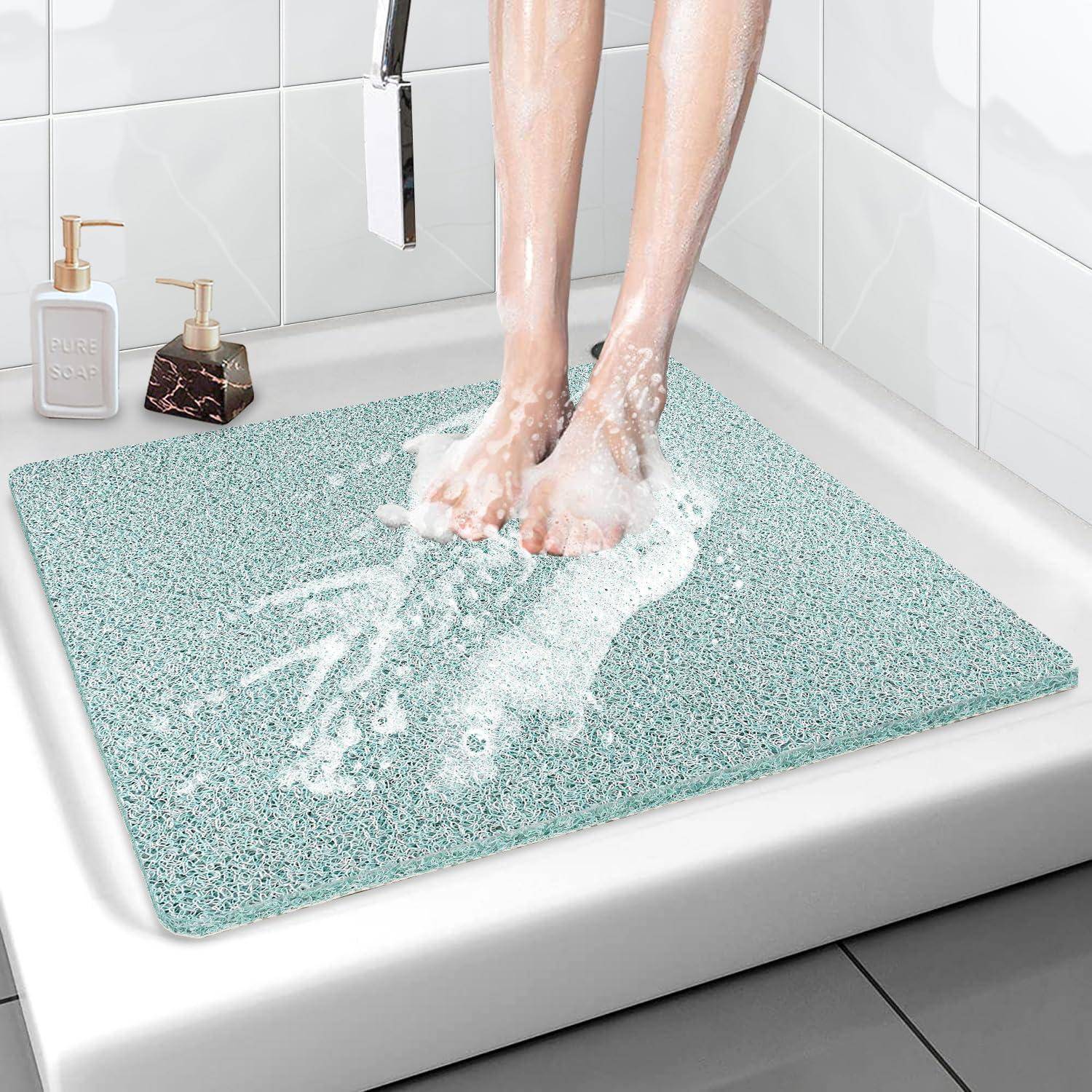 Füße stehen auf einer mintgrünen Badematte in einer Dusche, mit Wasser, das von der saugfähigen Matte in einem weiß gekachelten Badezimmer abprallt.