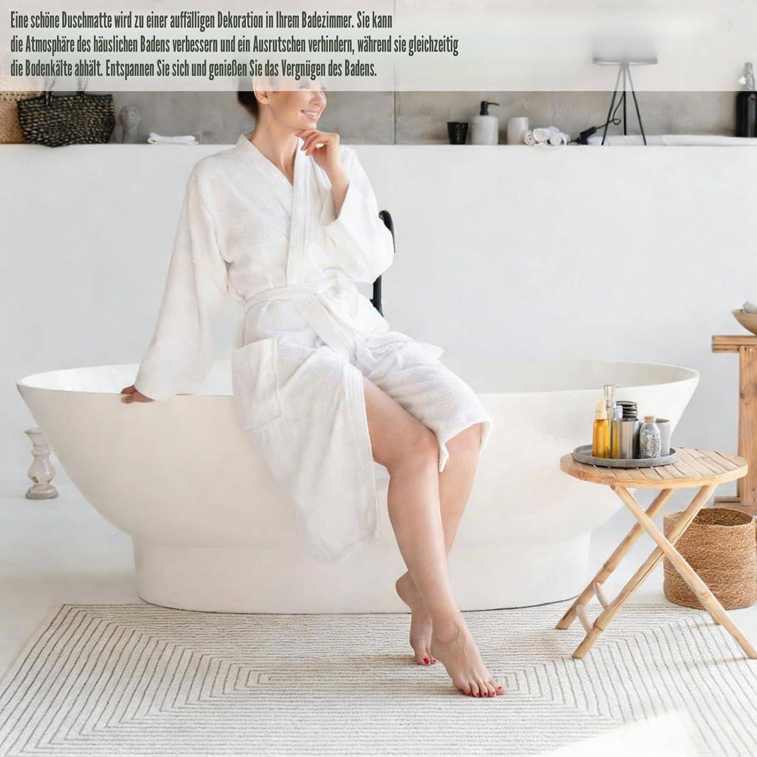Eine Frau in einem weißen Bademantel sitzt auf dem Rand einer freistehenden weißen Badewanne in einem hellen, minimalistischen Badezimmer-Spa-Setting.