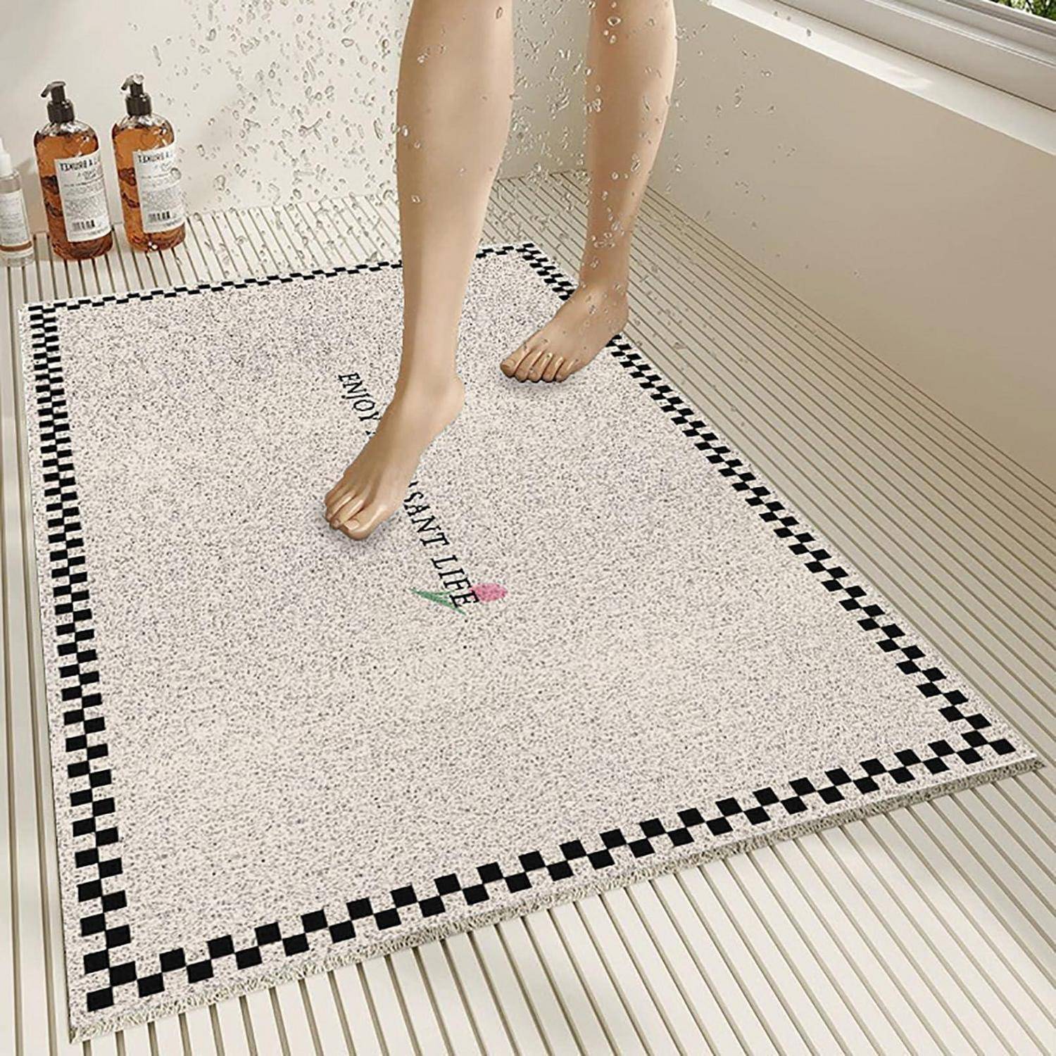 Ein Paar Schaufensterpuppenbeine steht auf einer gesprenkelten Badematte mit schwarzem karierten Rand, neben zwei Pumpflaschen neben einer Dusche.