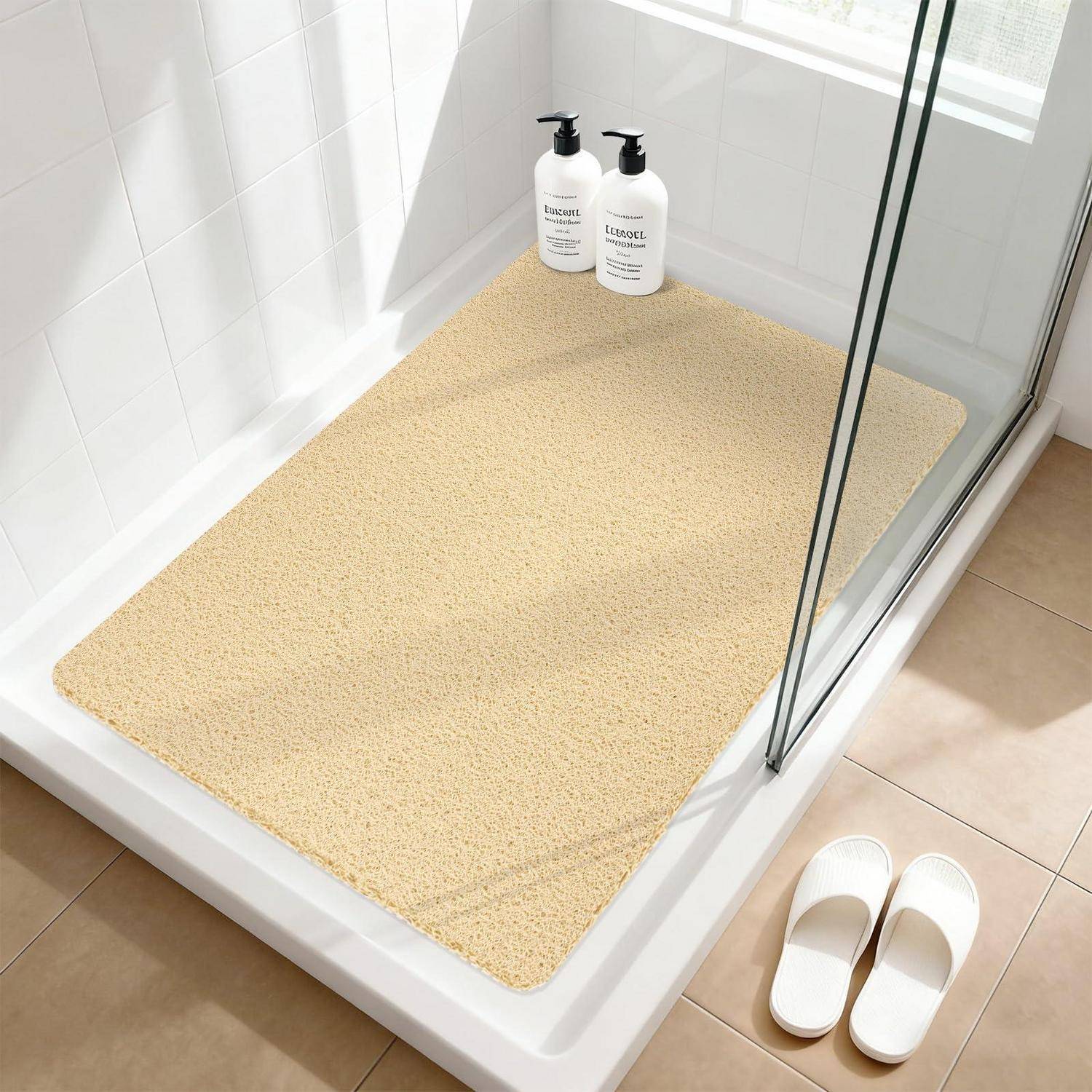 Badezimmerdusche mit einer beigen strukturierten Matte, zwei Pumpflaschen im Hintergrund und weißen Hausschuhen neben der Duschwanne.